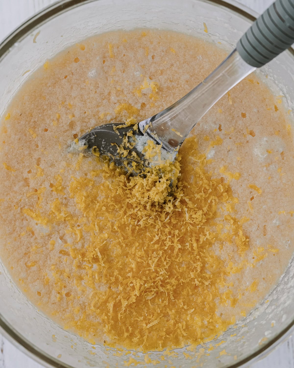 Overhead picture of glass bowl with ingredients mixed together and lemon zest on top and a spoon inside.