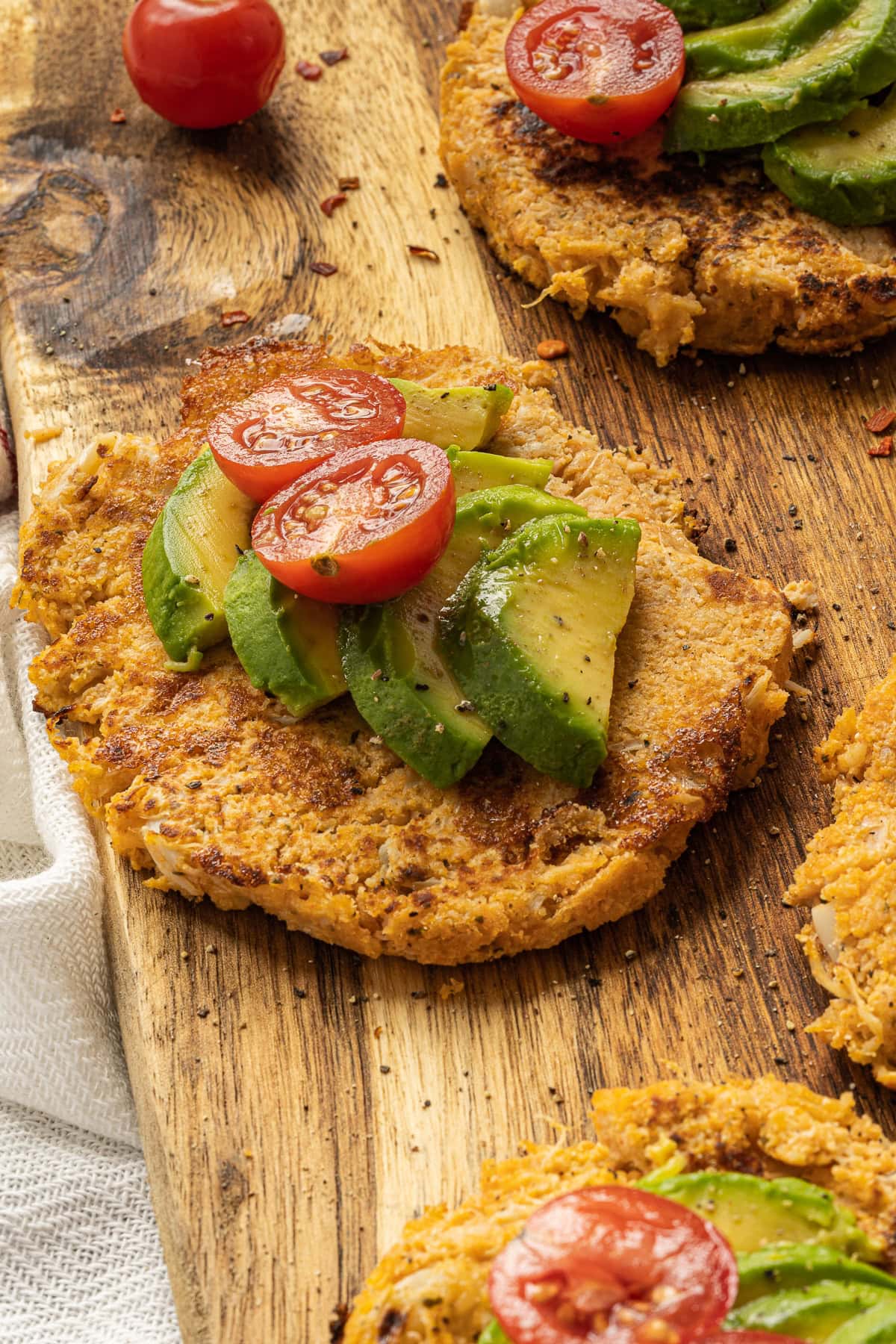 Close up picture of cauliflower fritters with sliced avocado and sliced tomatoes on top.