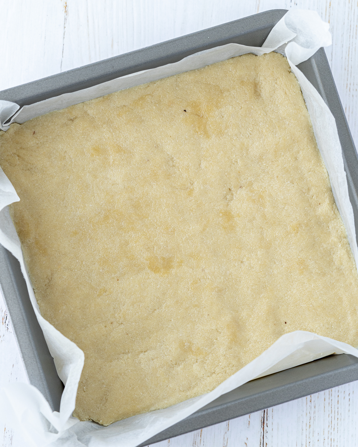 Overhead picture of dough of the crust in a rectangular baking tray lined with parchment paper.