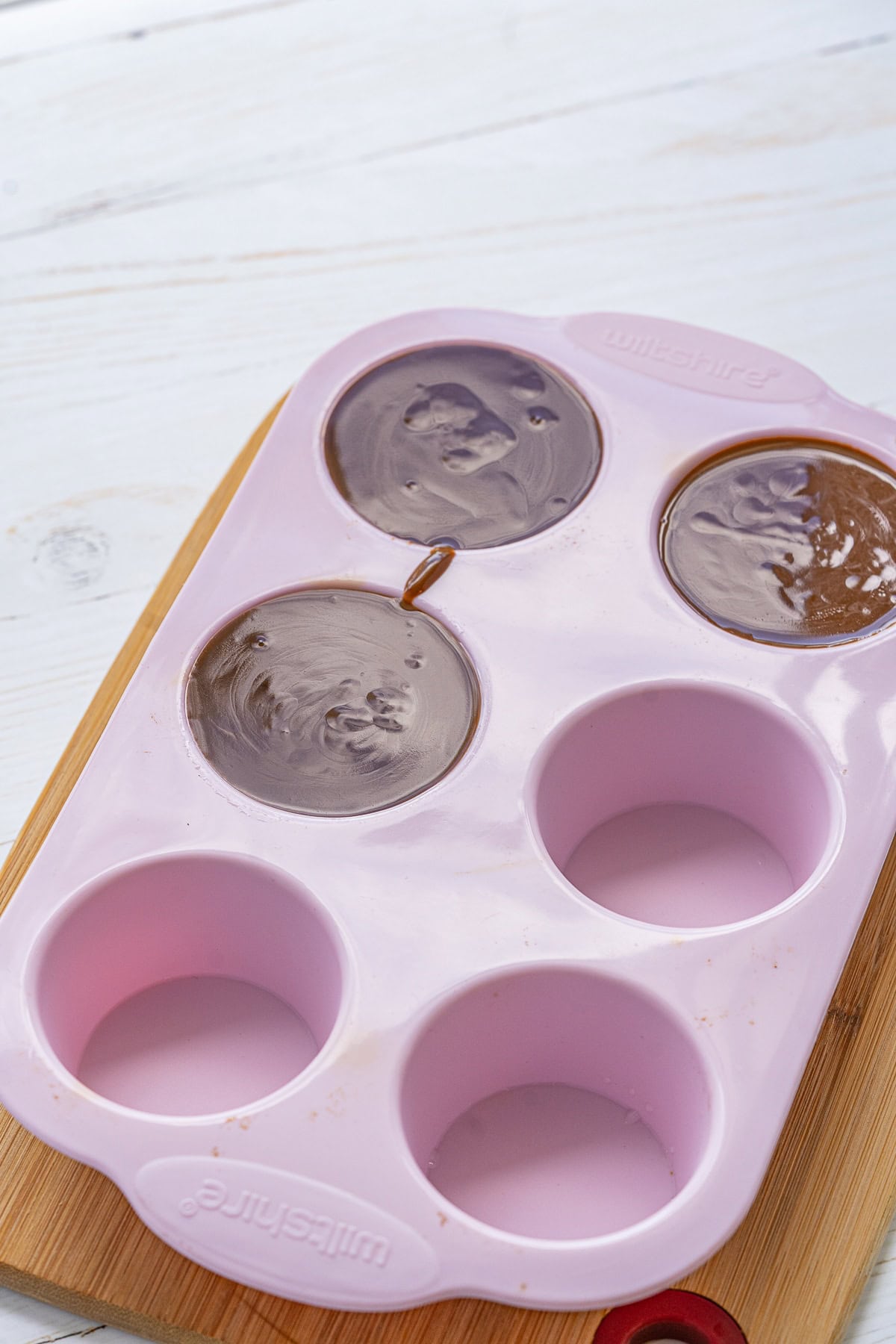 Picture of pink silicone molds on a wooden tray with three filled with batter for chocolate Panna Cotta.