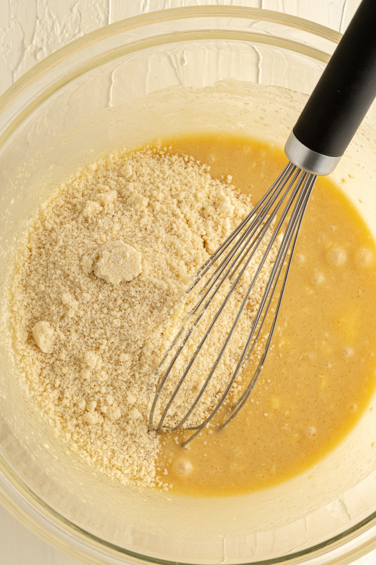 Close up picture of wet ingredients with almond flour in a glass bowl and whisk in it.