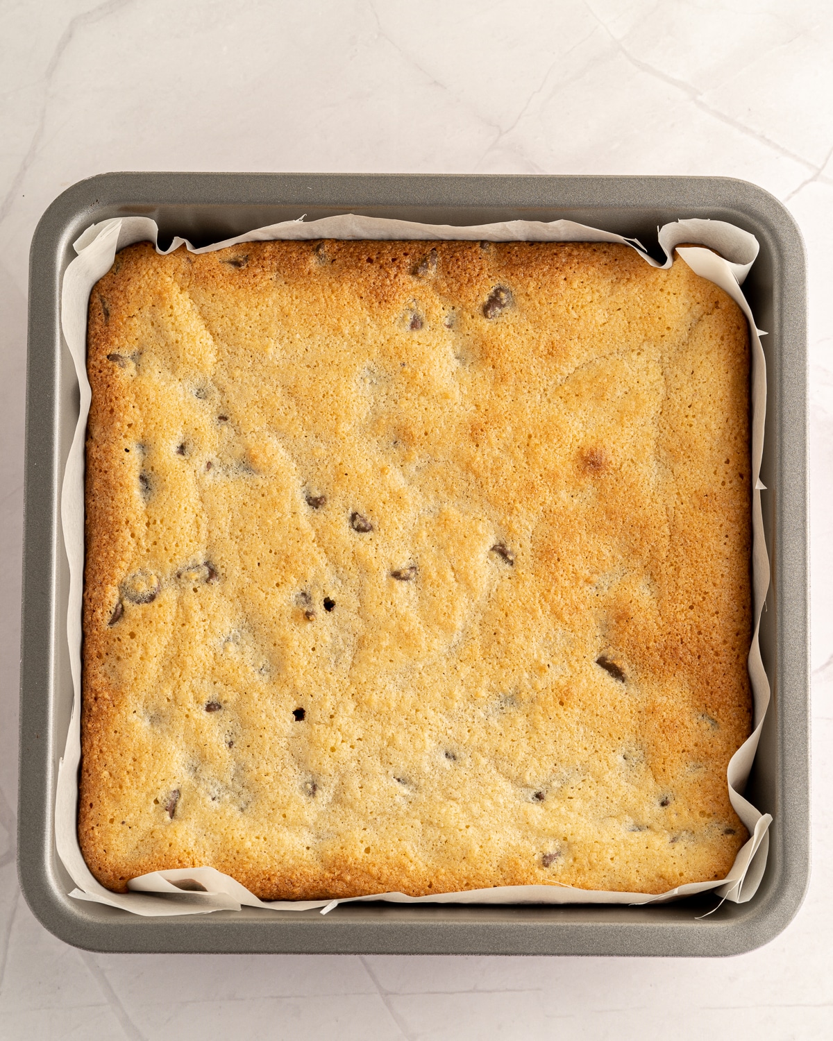 Overhead picture of cooked blondies uncut in prepared baking pan lined with parchment paper.