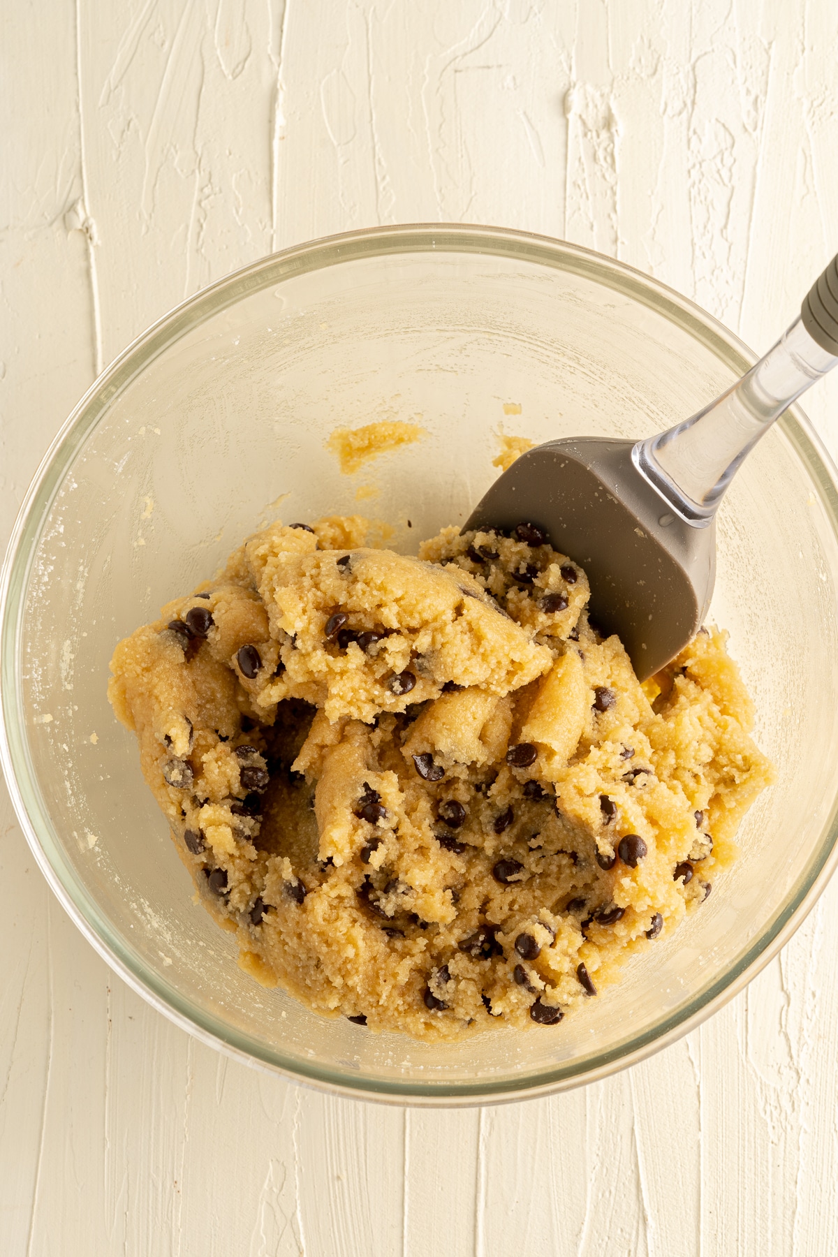 Overhead picture of chocolate chip blondie dough in a glass bowl with a large metal spoon in there.