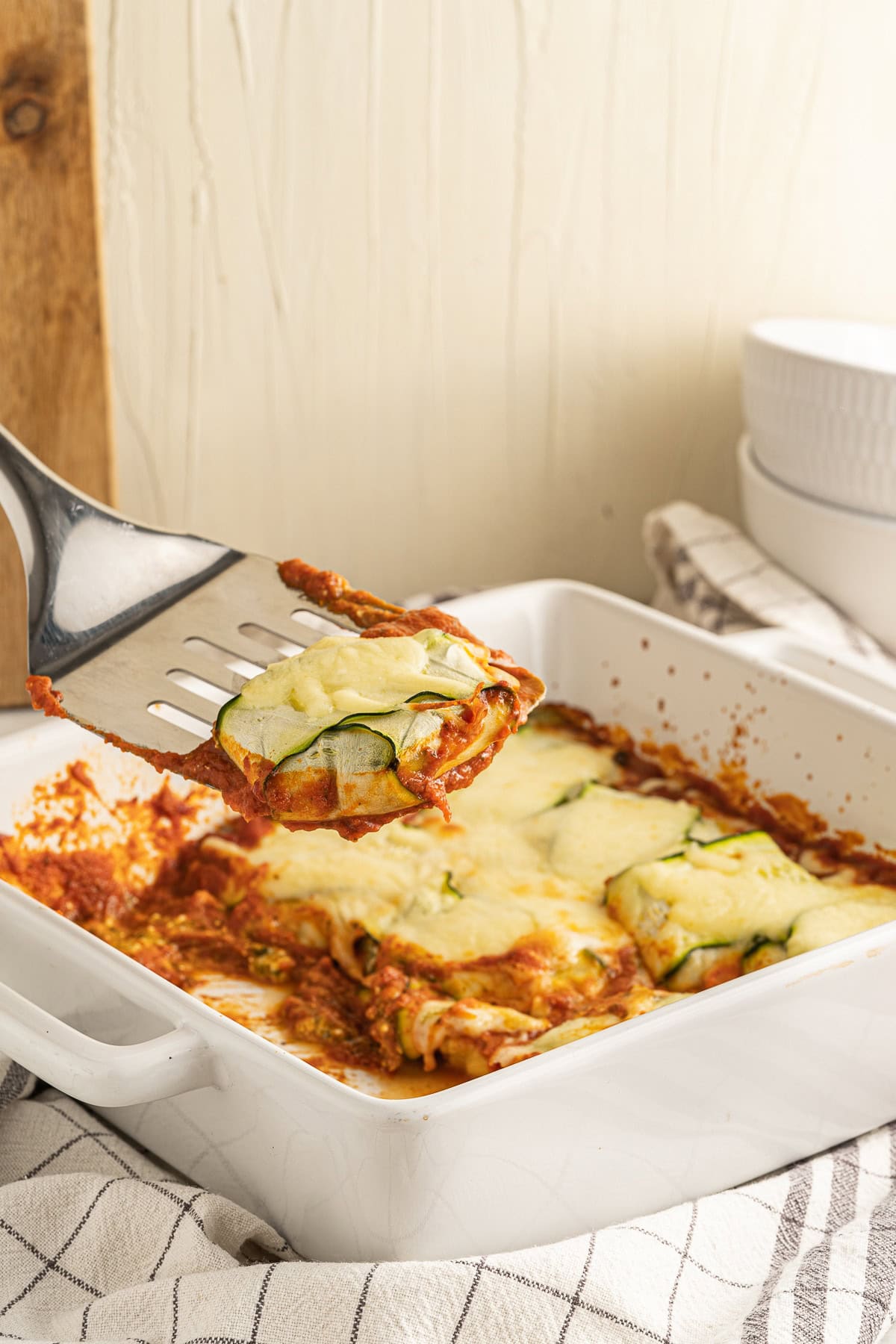 Picture of zucchini ravioli in a white square baking dish with one piece of ravioli on a steel spatula above the baking dish.