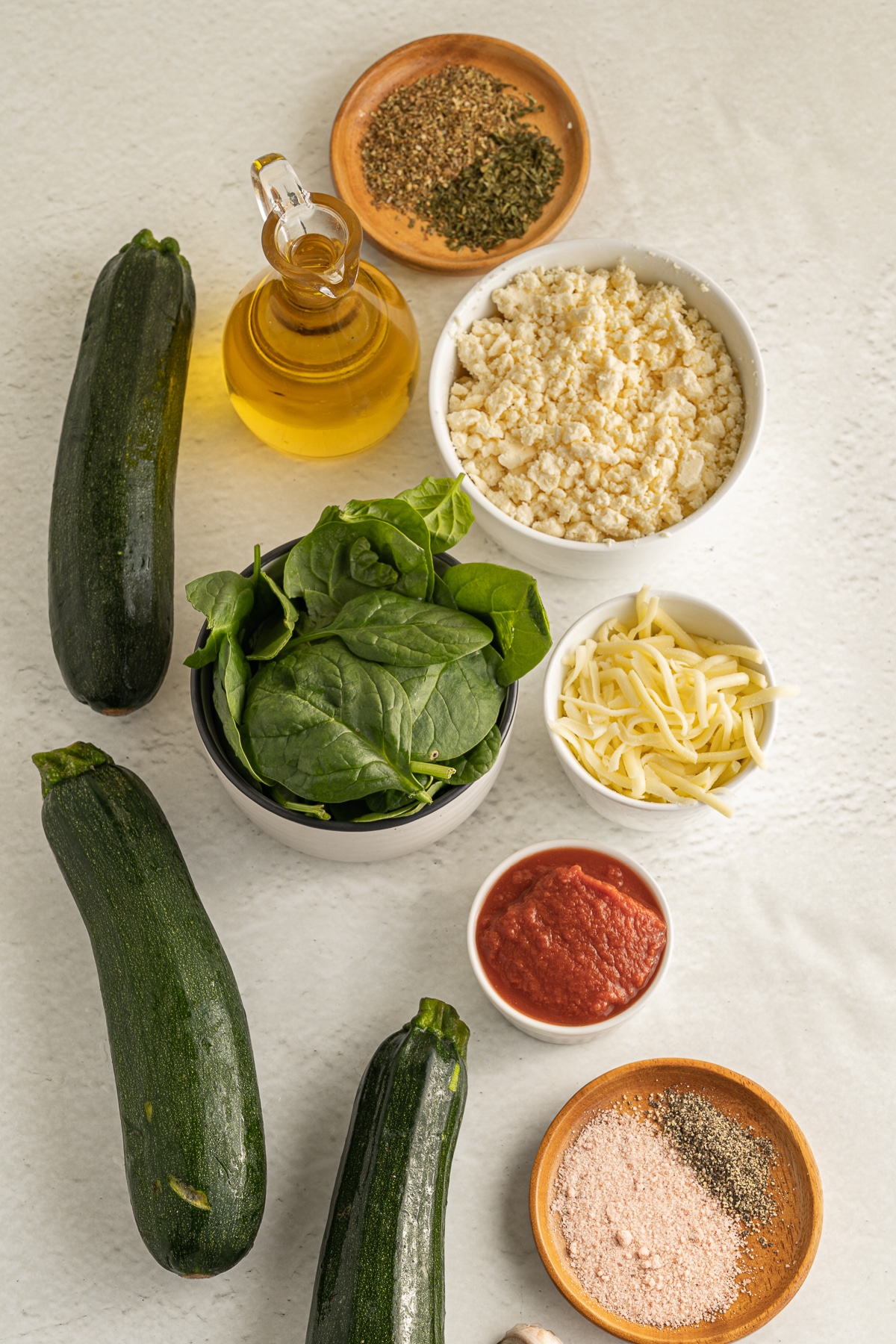 Overhead picture of all the ingredients for zucchini ravioli on a white background, all in separate white bowls or directly on the background.