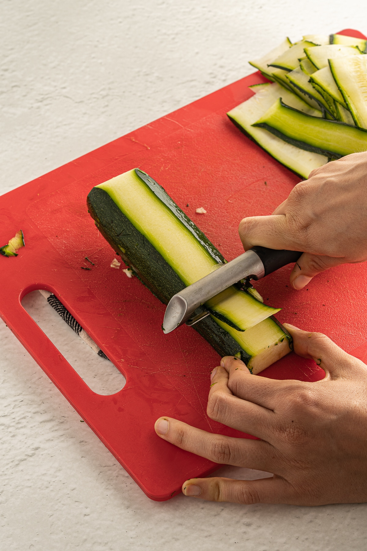 Picture of two hands grating zucchini on a red cutting board.