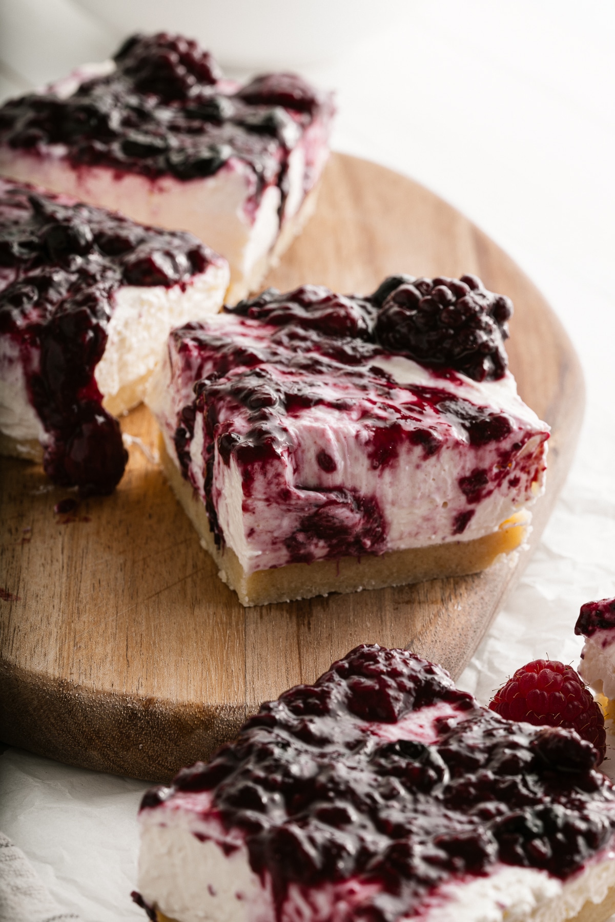 Picture of four berry cheesecake bars on a wooden platter with berry topping and fresh berries on top.