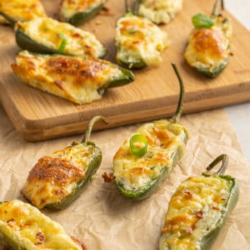 Finished picture of Jalapeño Poppers recipe n parchment in the front and more jalapeño poppers on a wood cutting board in the back.