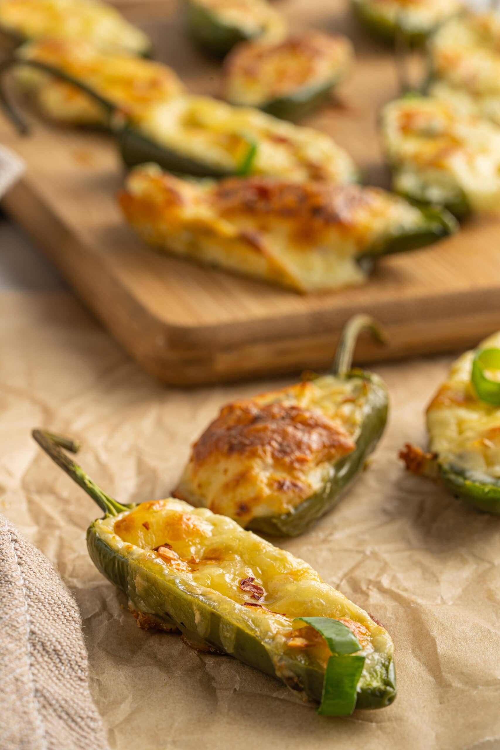 Close up picture of cooked jalapeño poppers recipe in the front and other poppers in the back on a wood cutting board.