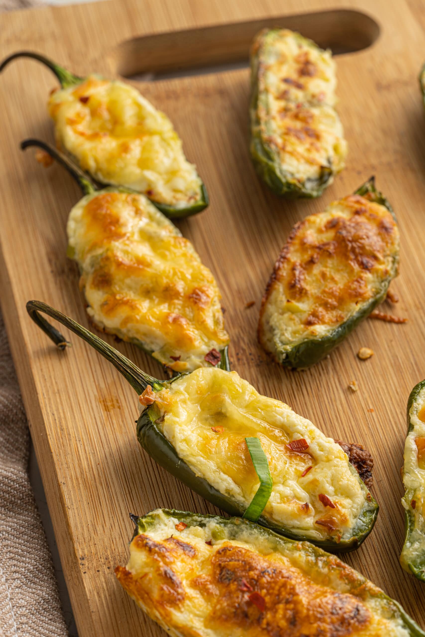 Cooked jalapeño poppers recipe with browned melted cheese on top on a wooden cutting board.