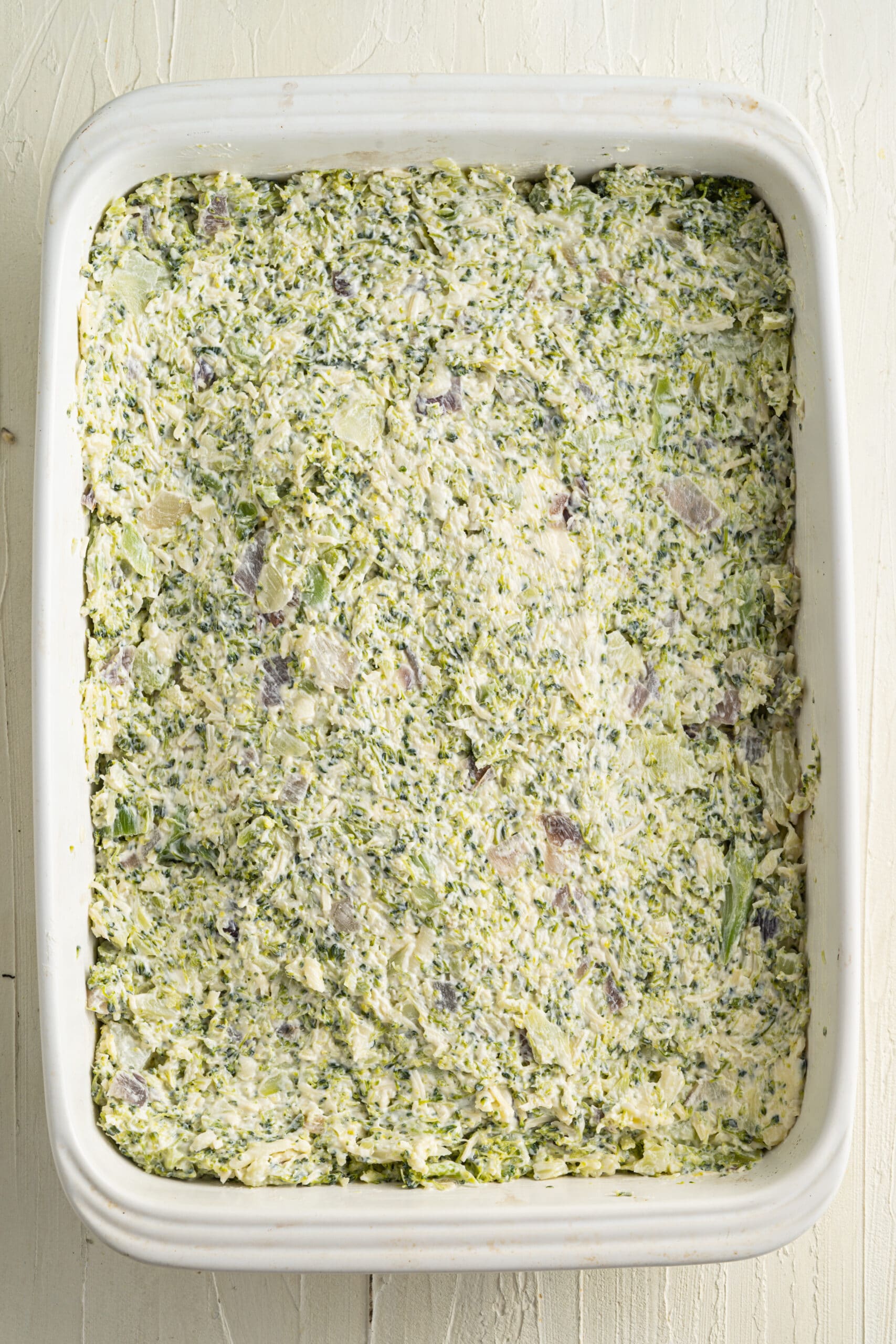 Overhead picture of uncooked broccoli cheese mixture in a white rectangular baking dish.