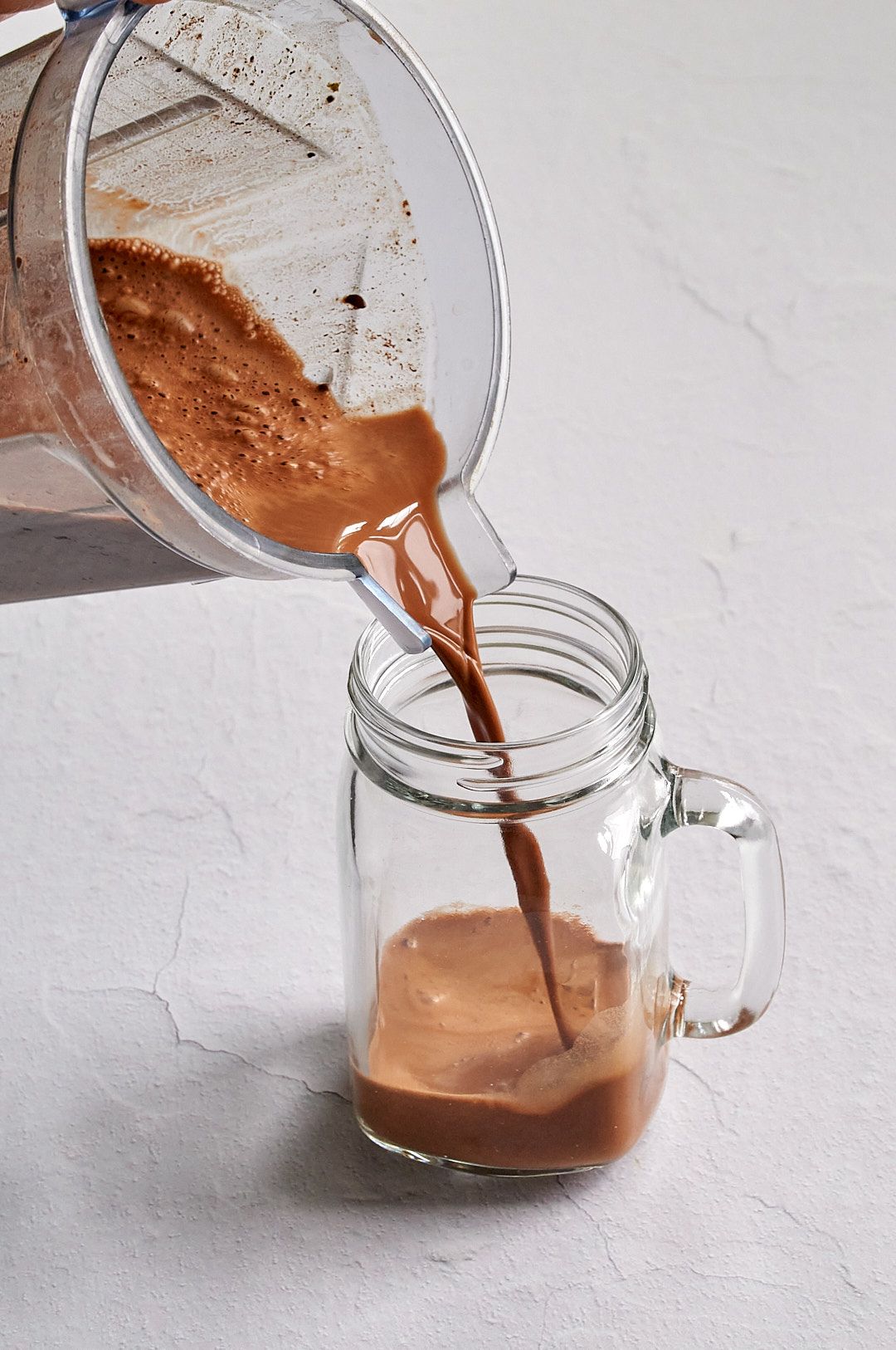Picture of the hot chocolate being poured from a clear blender into a clear glass mason jar mug.