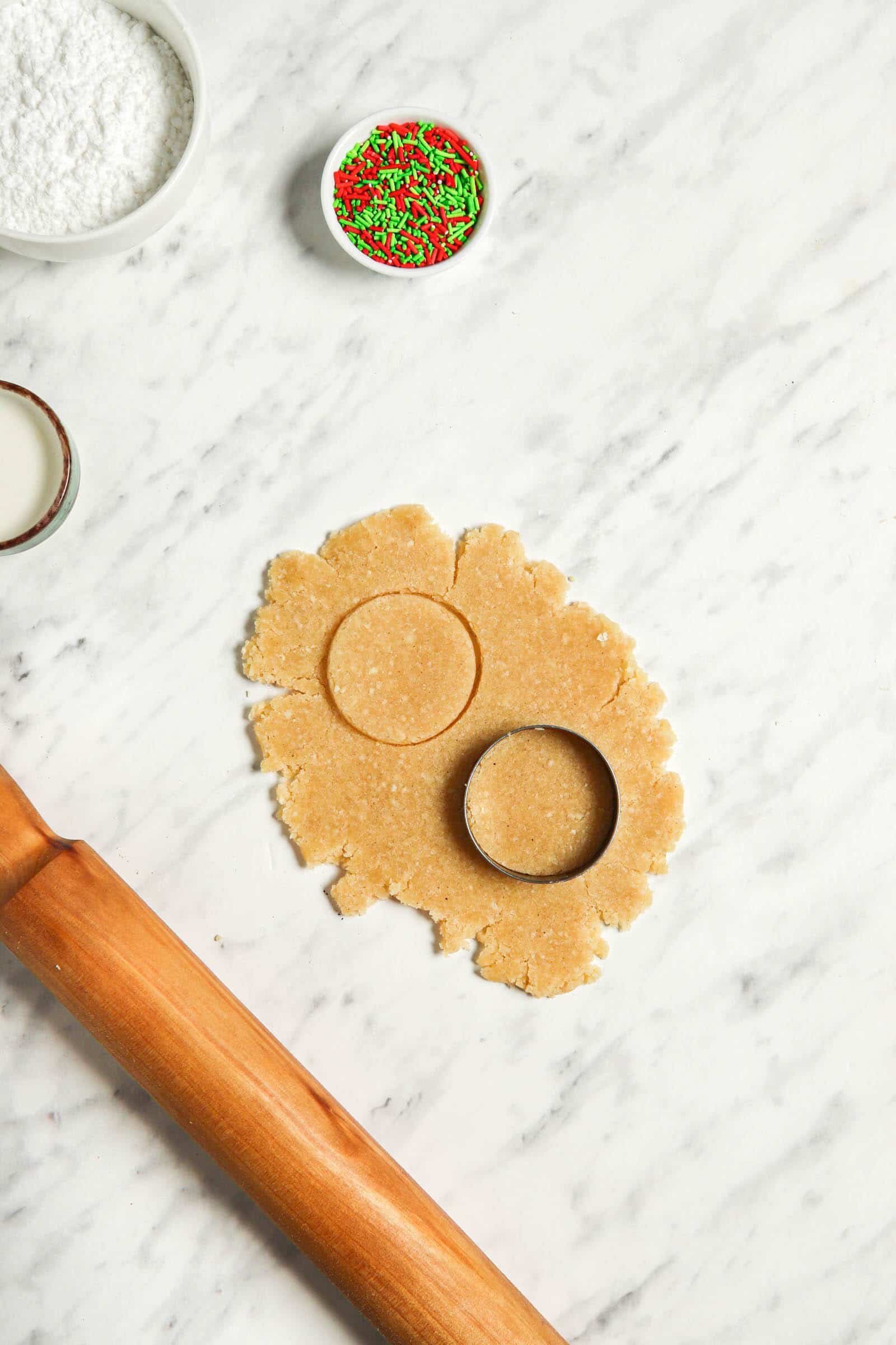 Dough for iced sugar cookies on a white background with cookie cut outs and a rolling pin.