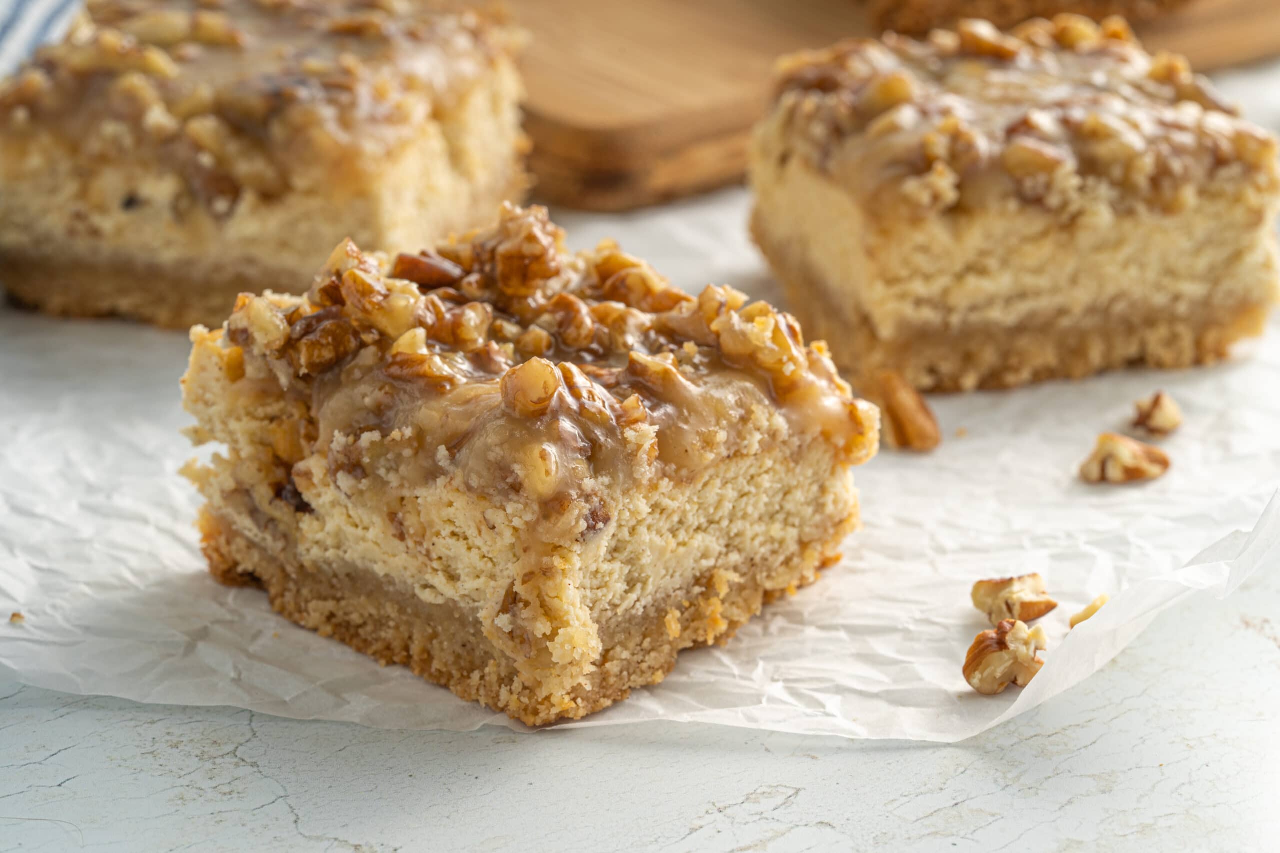 Close up horizontal picture of three pecan cheesecake bars on parchment paper.