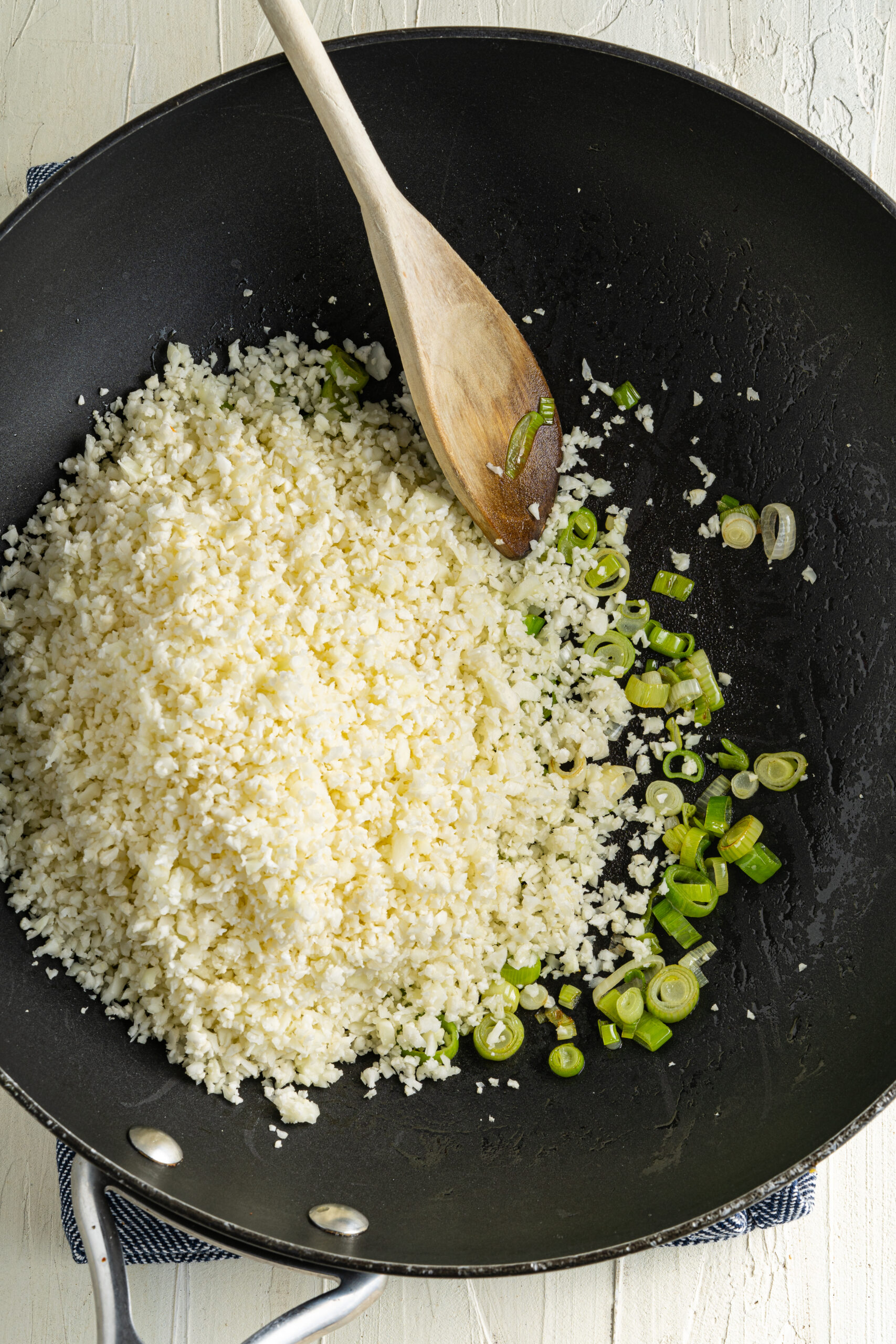 Cauliflower rice and chopped green onion in a skillet.