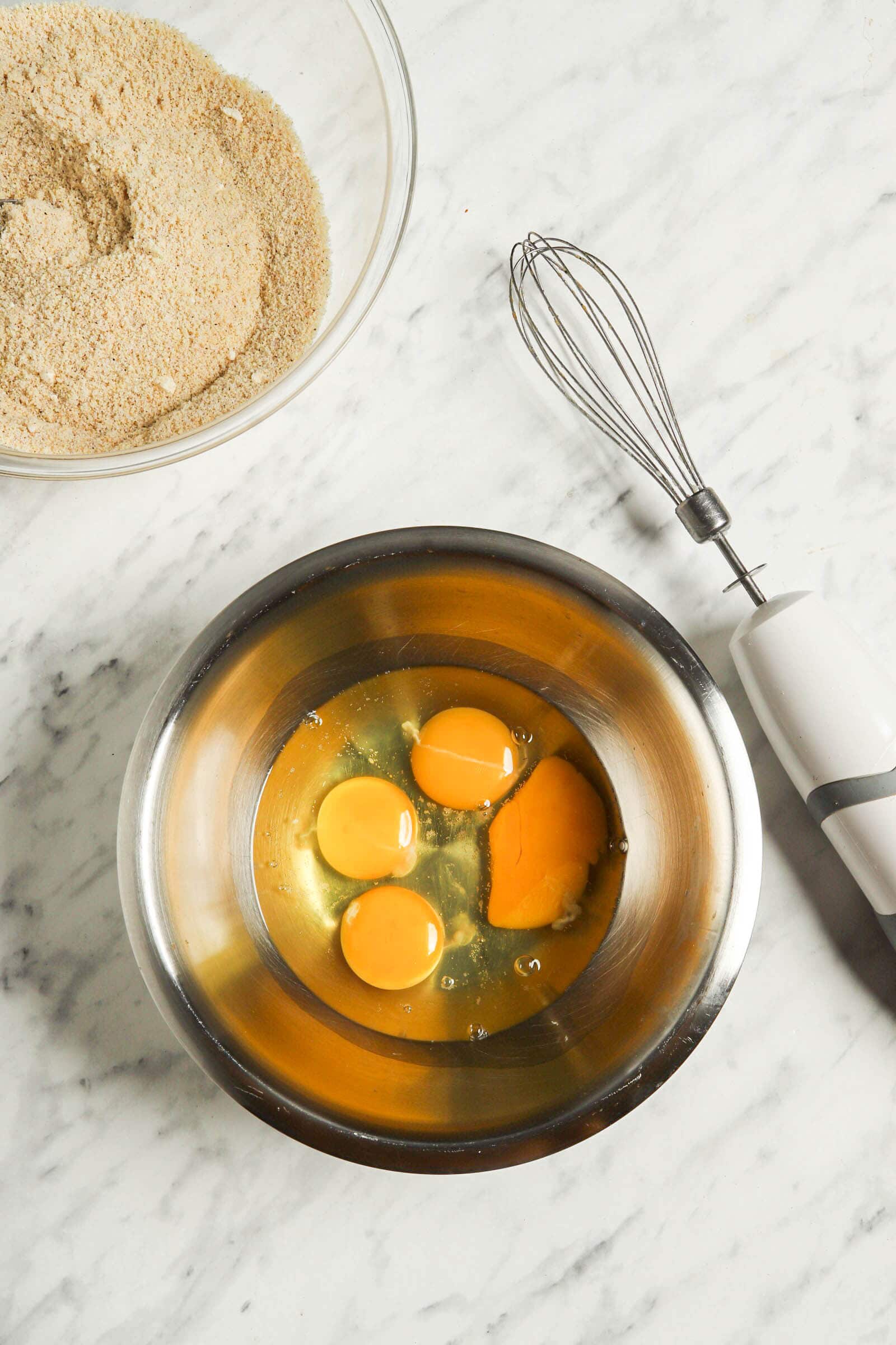 Picture of eggs in steel bowl with a whisk next to it.