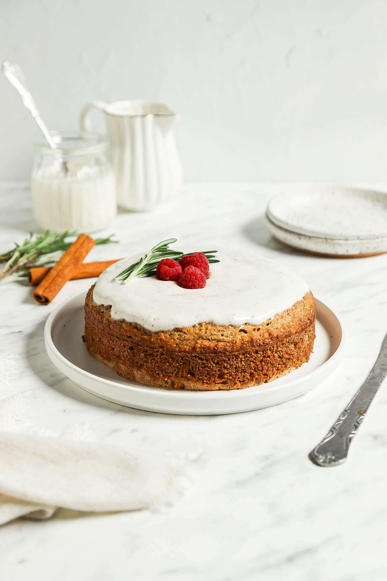 Gingerbread cake with frosting and berries on top on a white plate.