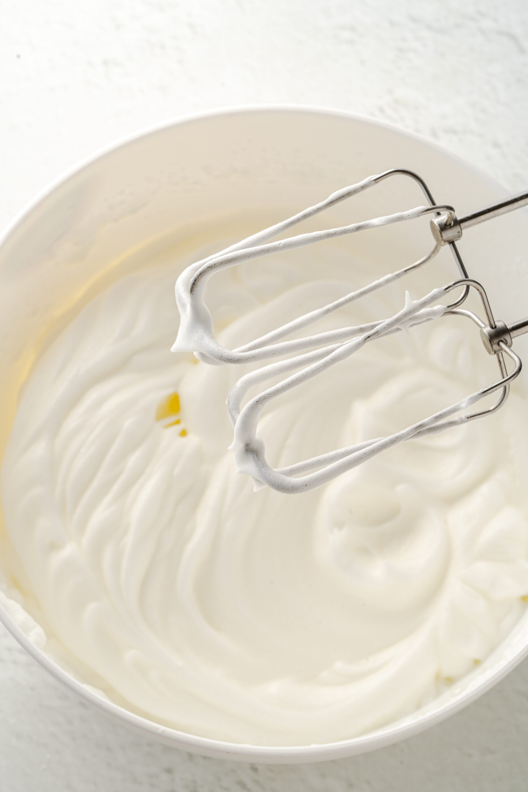 Whipped egg whites in a mixing bowl with electric mixer in it.