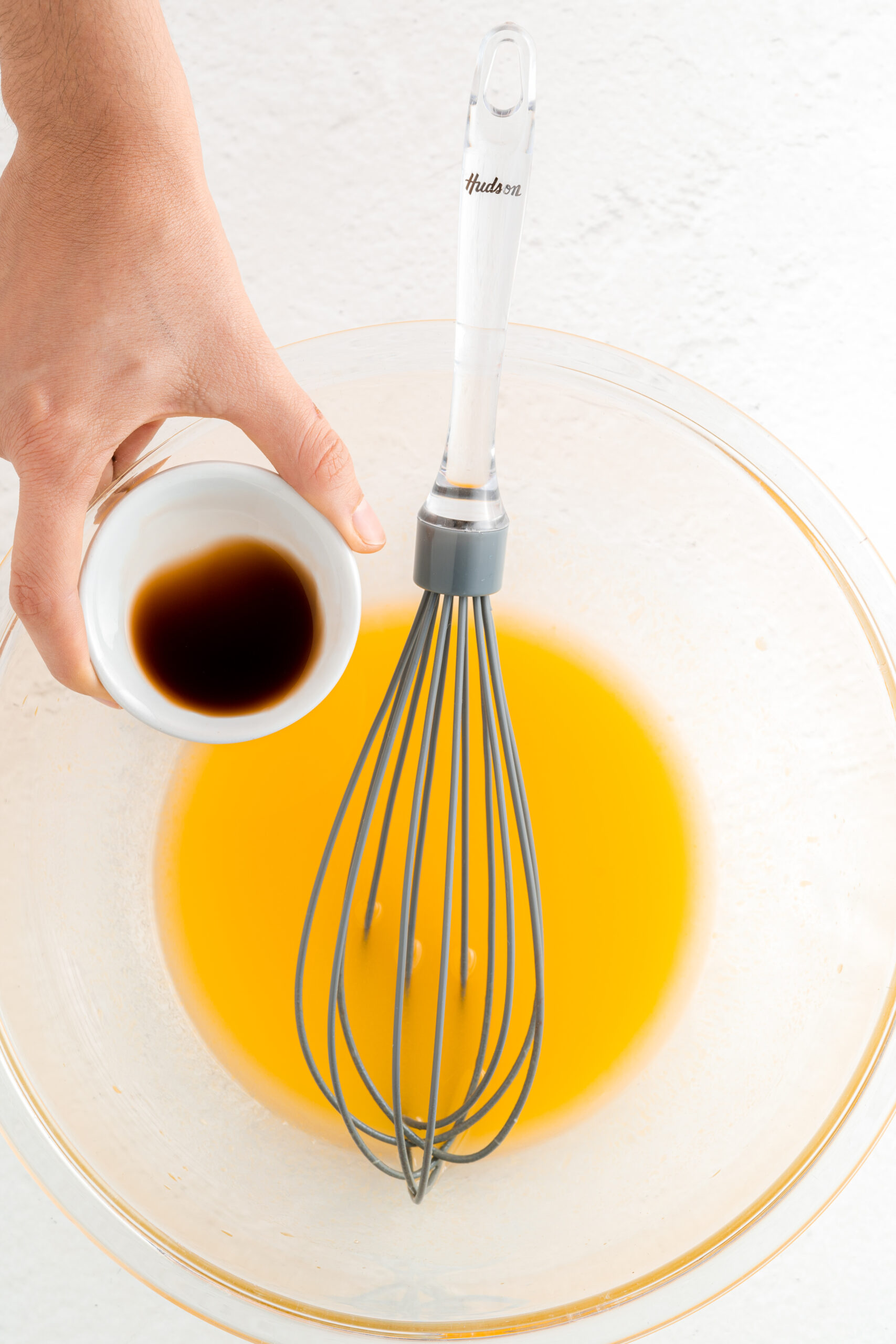 Glass mixing bowl with wet ingredients and a whisk.