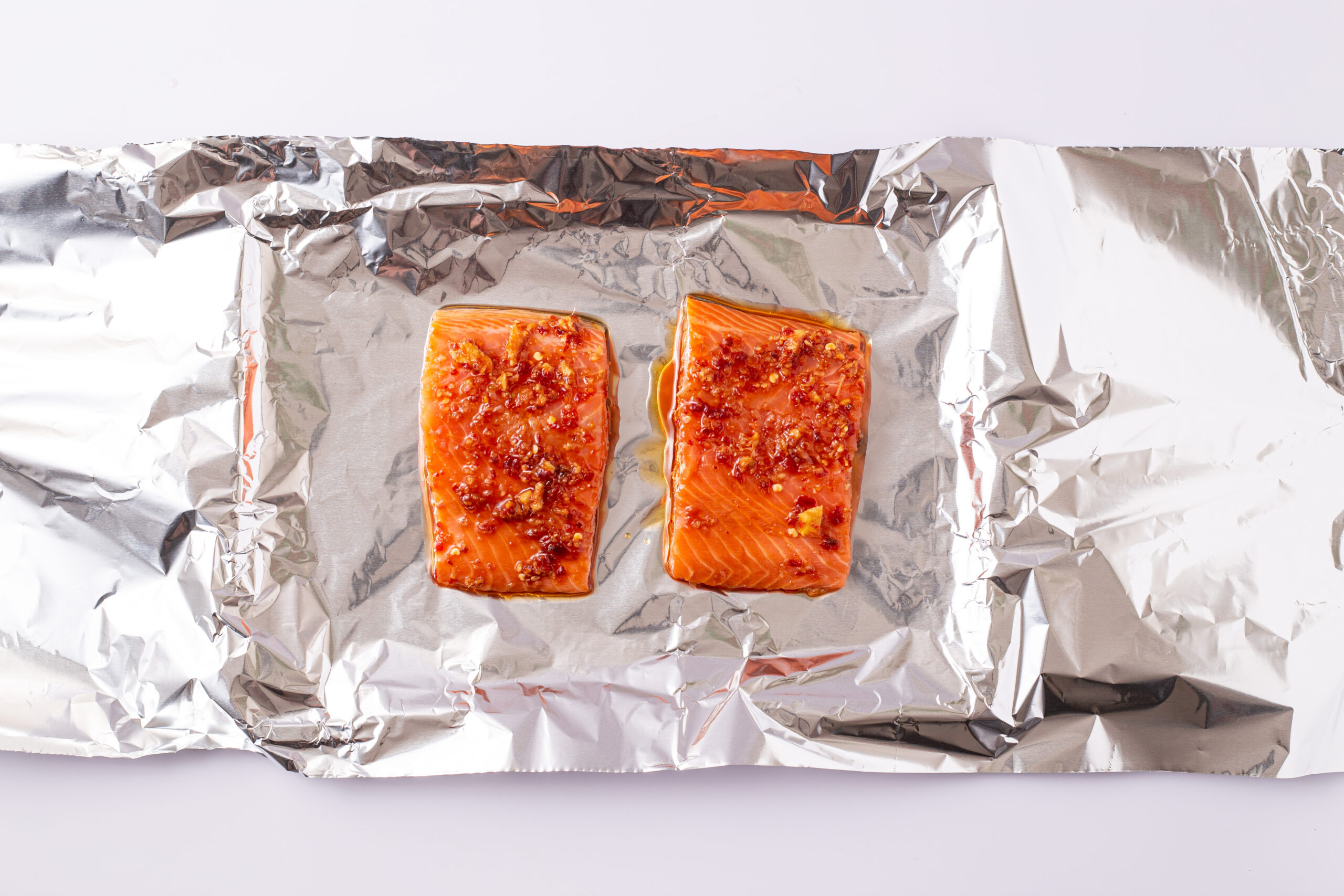 Prepared salmon on an aluminum foil lined baking sheet.