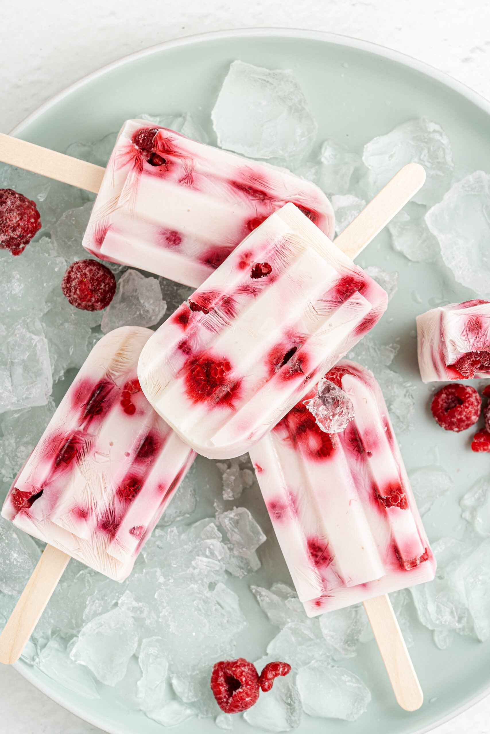 Raspberry yogurt popsicles on a plate of ice.