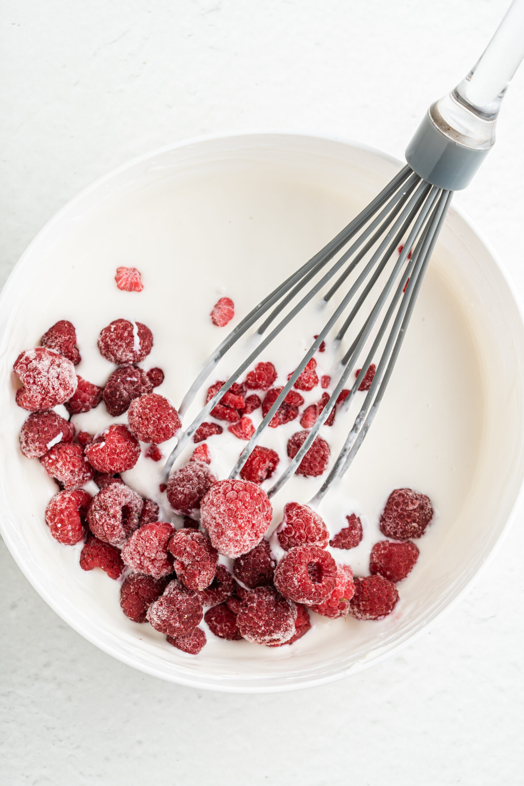 Adding raspberries to yogurt mixture in mixing bowl.