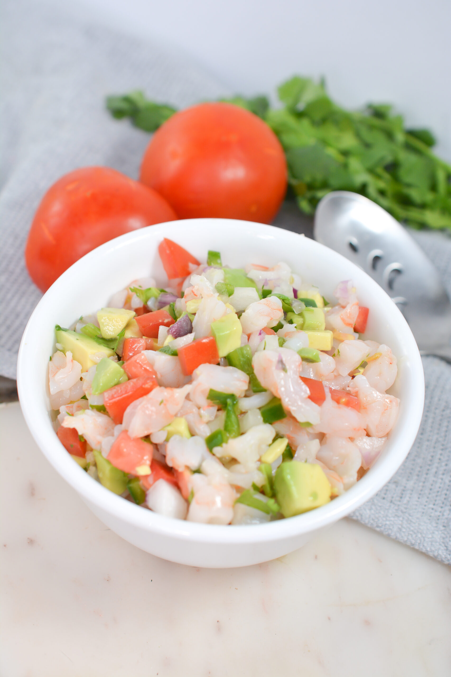 Shrimp ceviche in white bowl with tomatoes above the bowl.