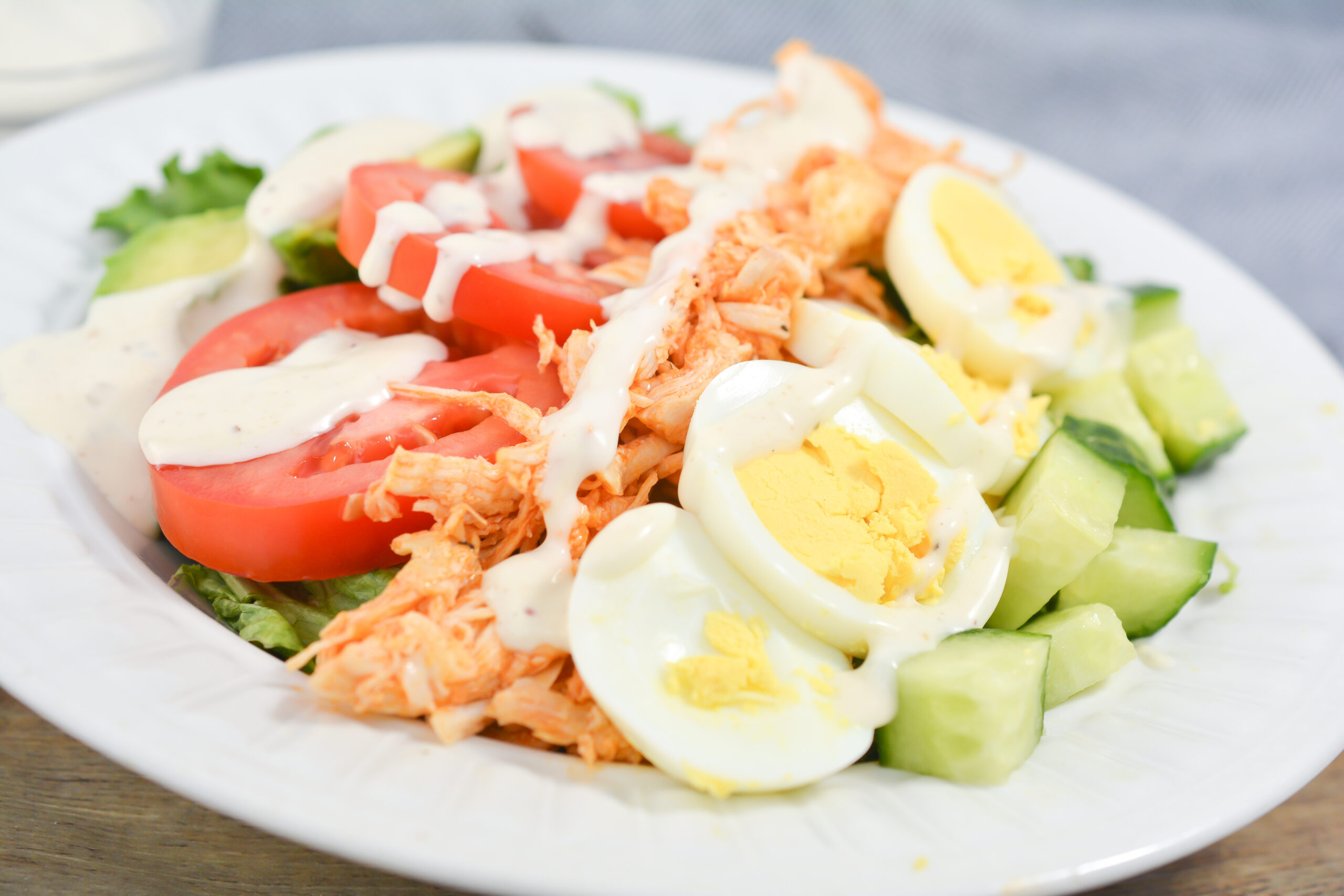 Buffalo Chicken Cobb Salad on a white plate with dressing on top.