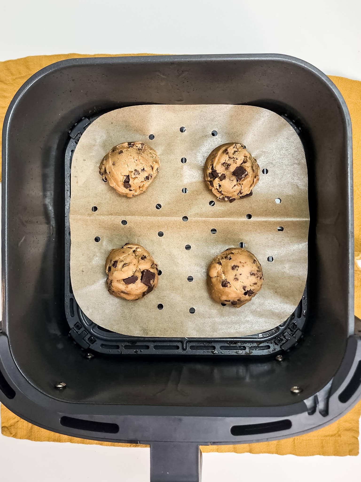 Chocolate chip cookie dough in air fryer on parchment lined basket.