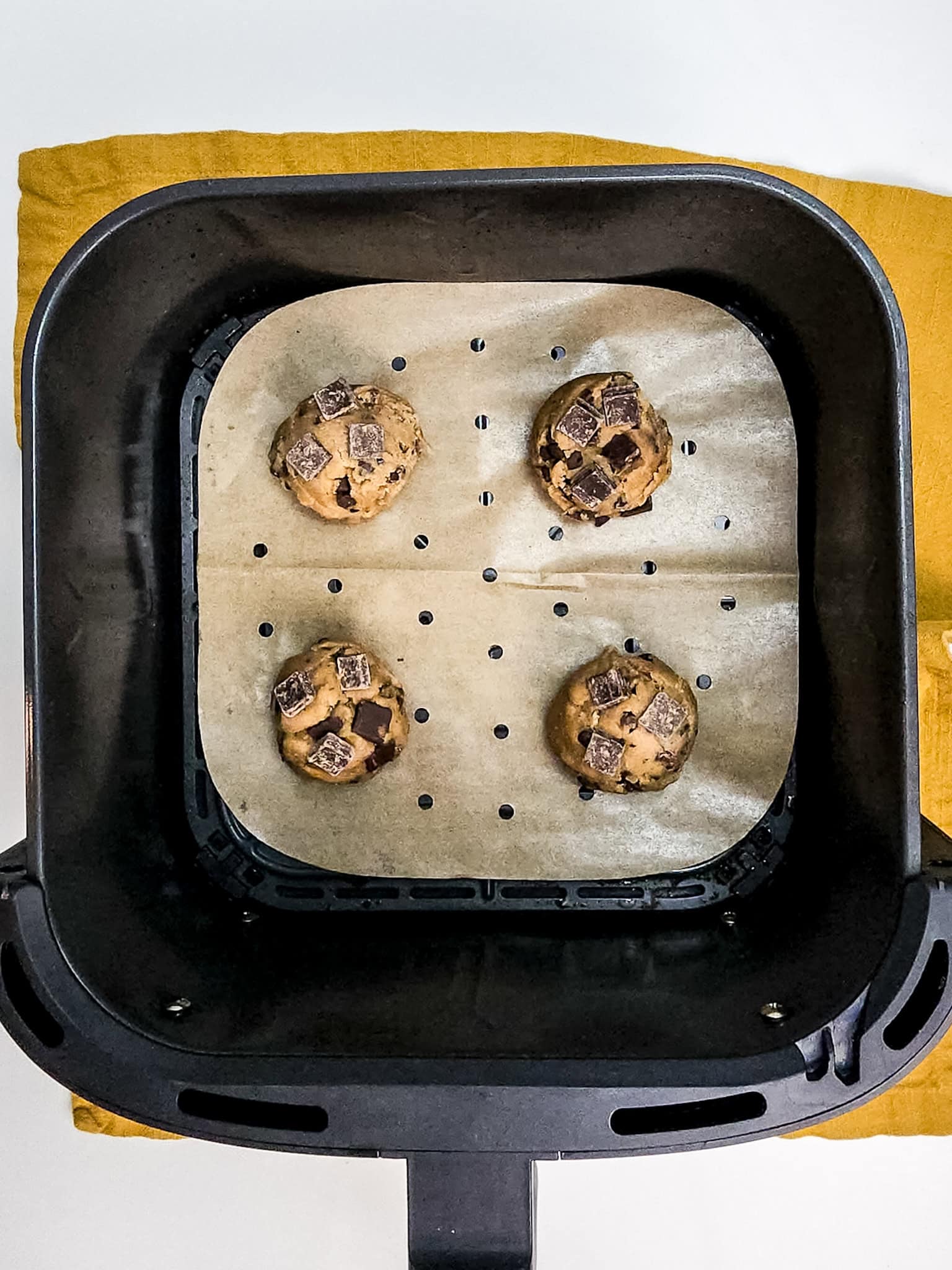 Chocolate chip cookie dough with chunks in air fryer on parchment lined basket.