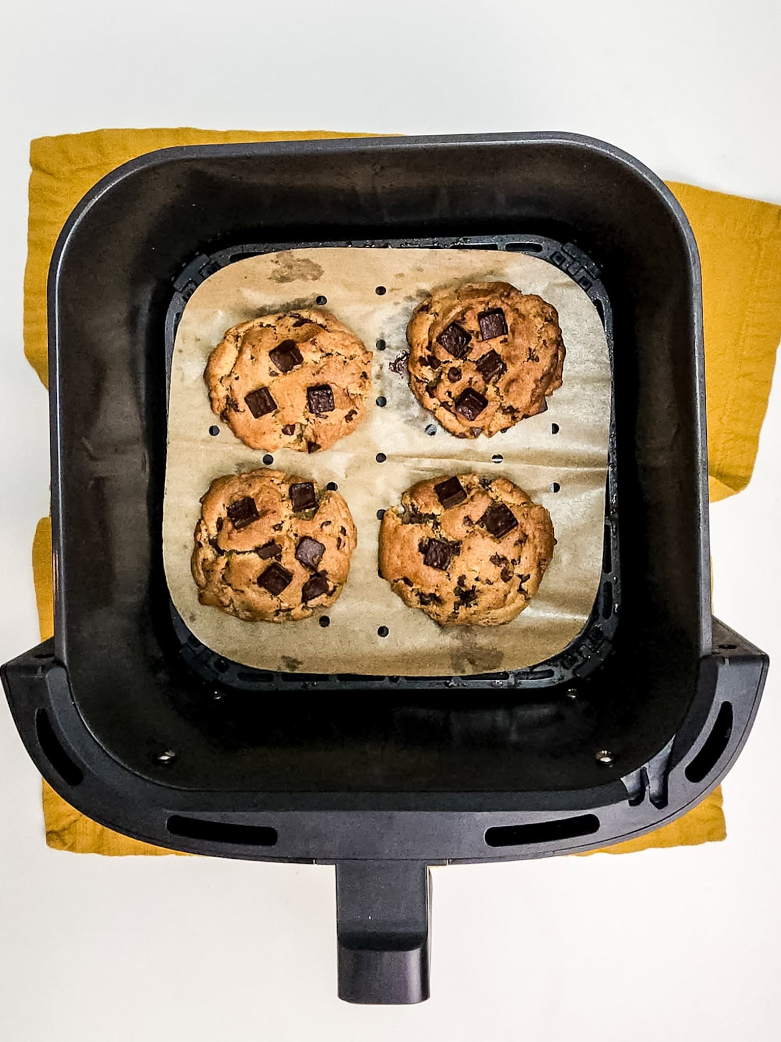 Chocolate chip cookies in air fryer on parchment lined basket.