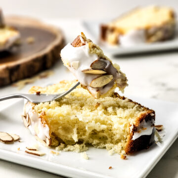 A slice of Greek yogurt almond cake on a white plate with a fork in it.