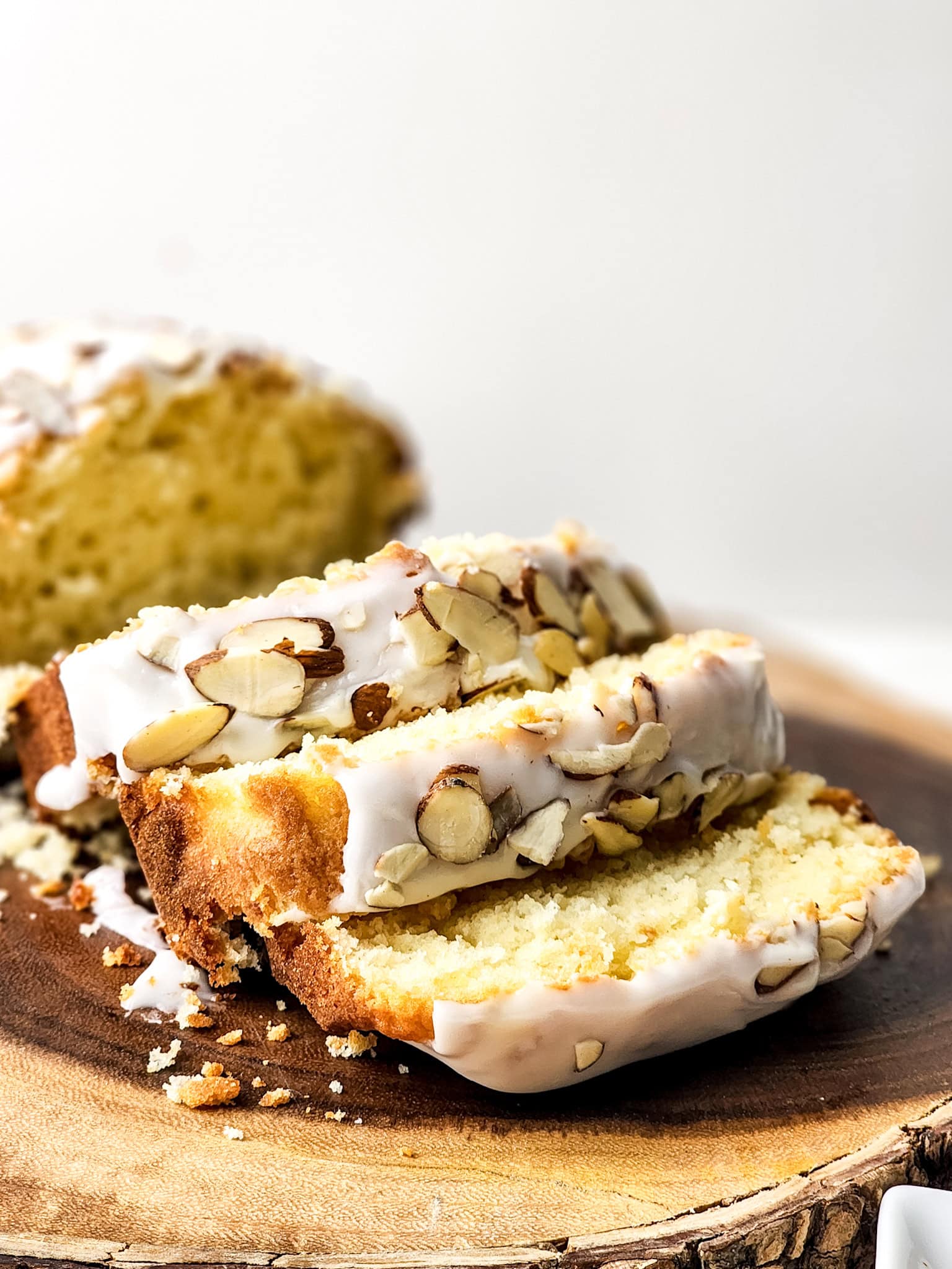 Slices of Gluten Free Greek Yogurt Almond Cake topped with a light almond glaze and sliced almonds, served on a wood tray.