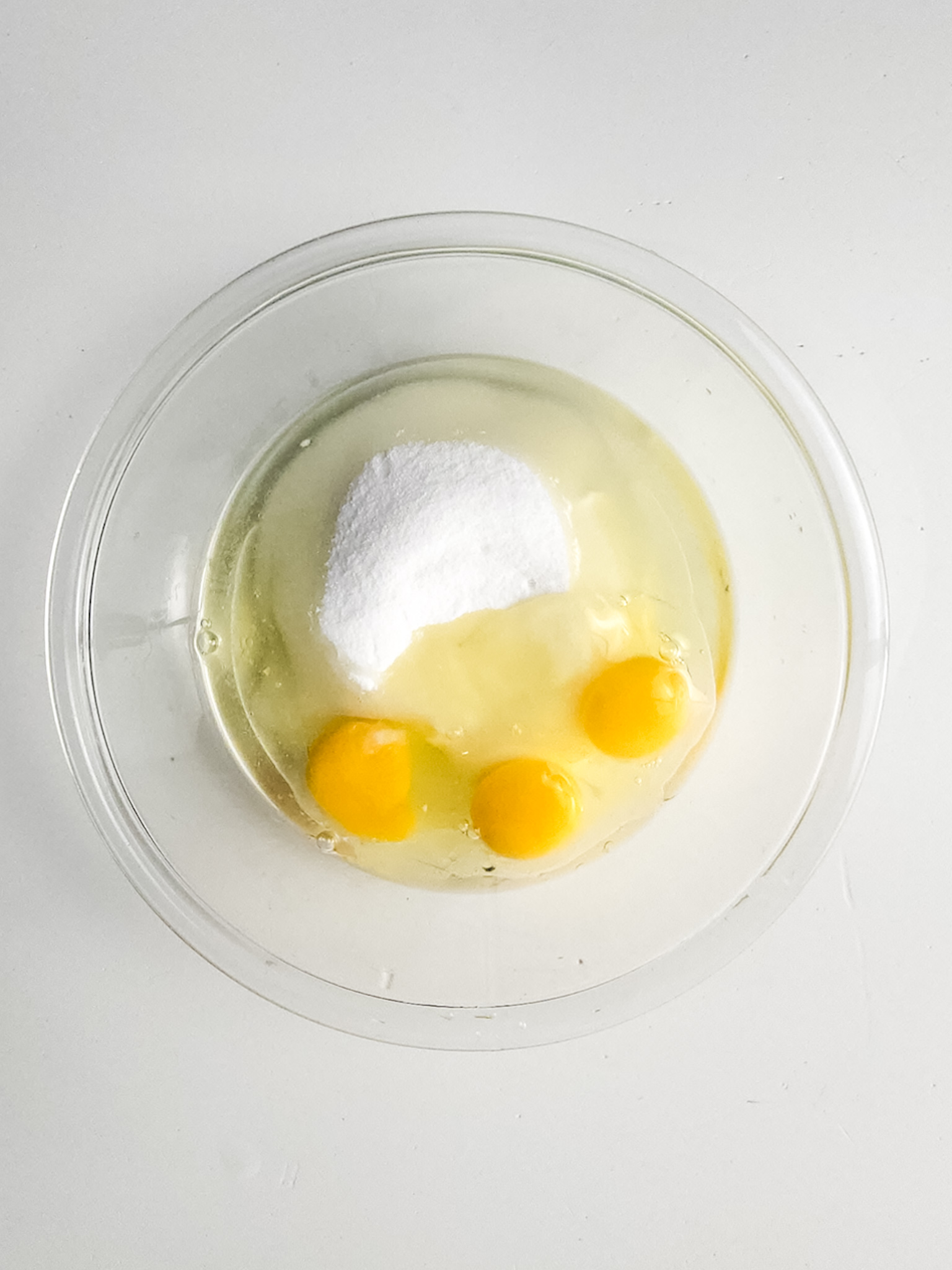 Yogurt, vanilla, oil, sugar, eggs and almond extract in a glass bowl.
