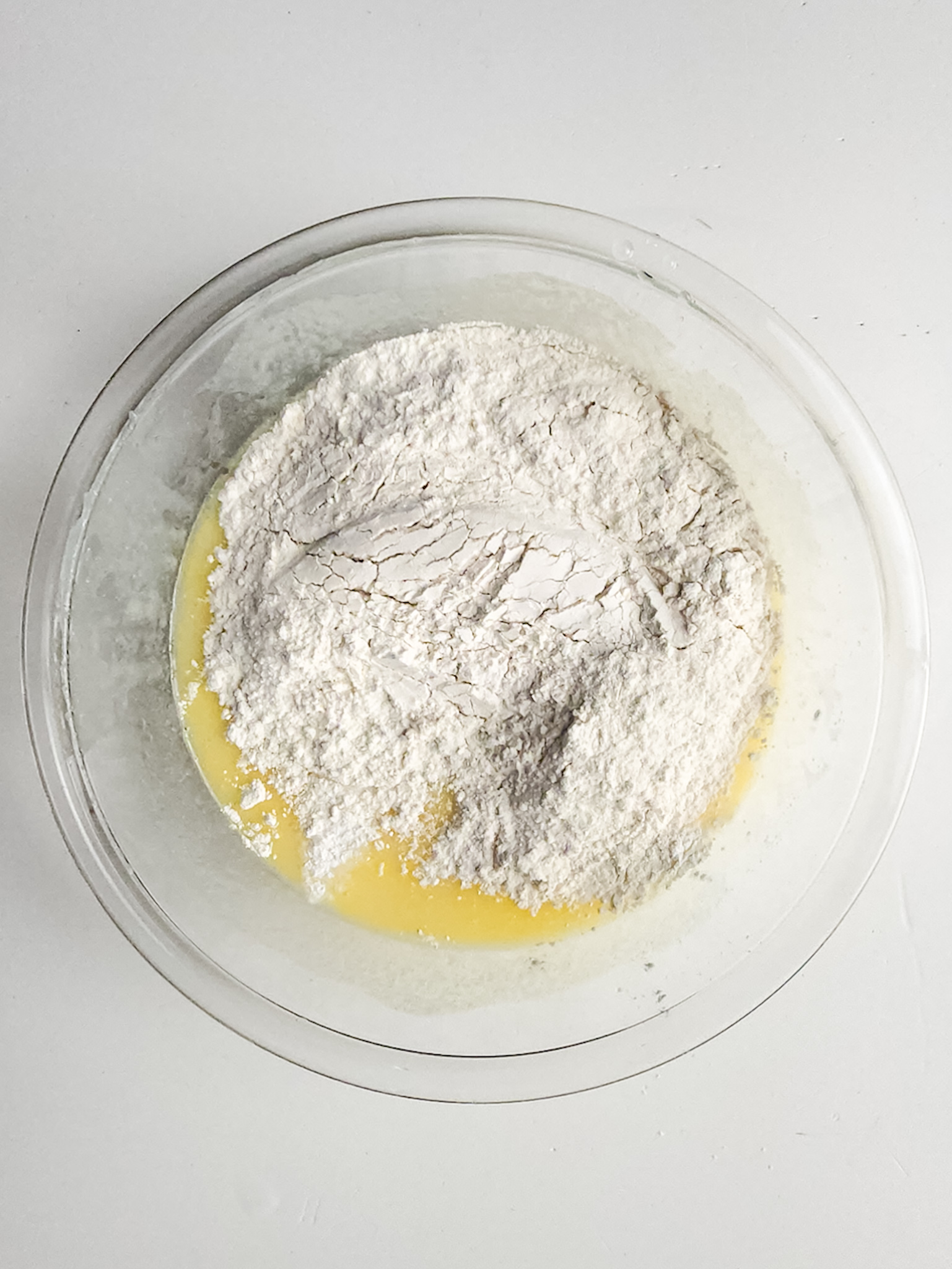 Yogurt, vanilla, oil, sugar, eggs, baking powder, flour and almond extract in a glass bowl.