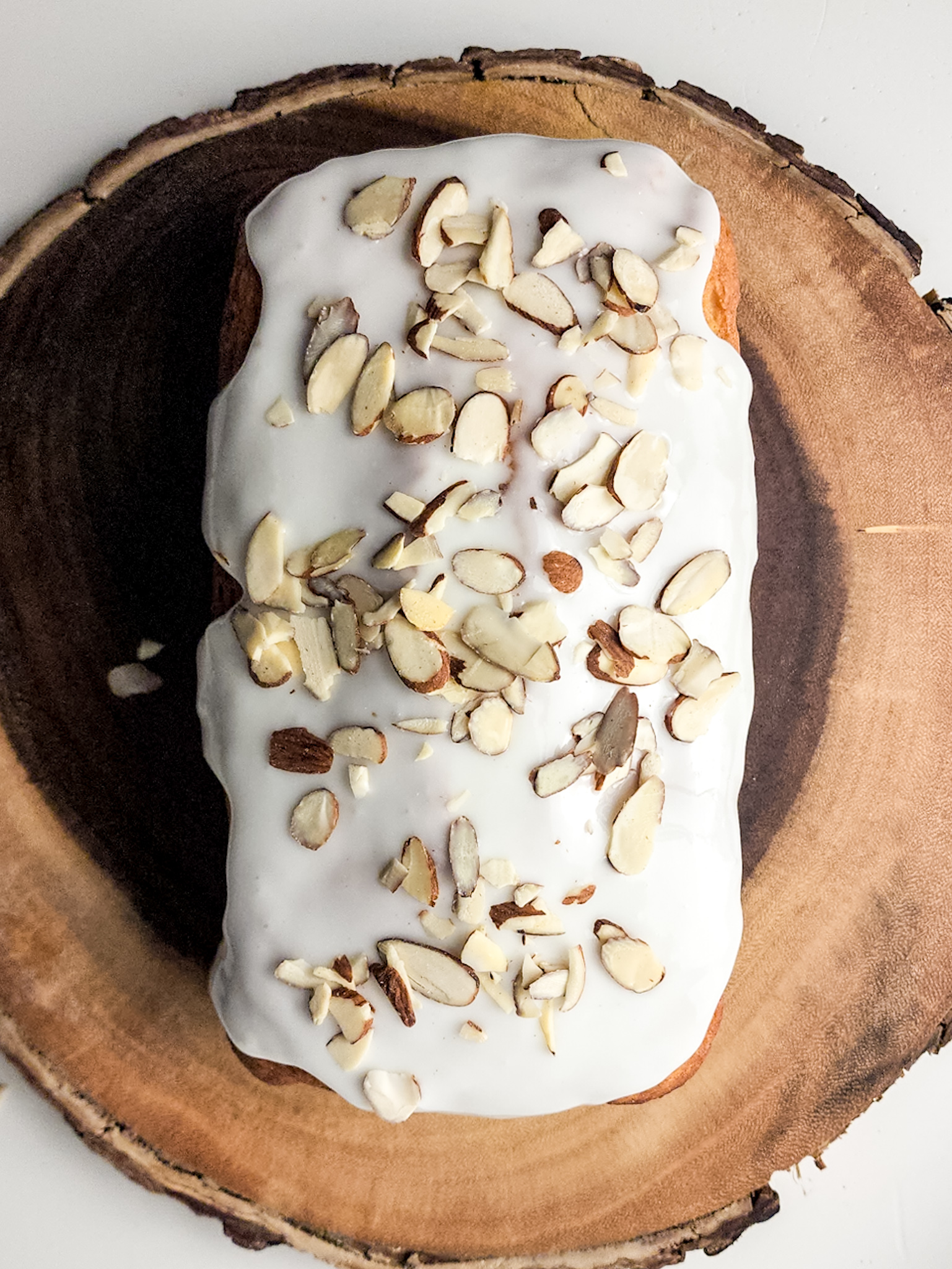 Almond glazed cake with sliced almonds on top on a wood tray.