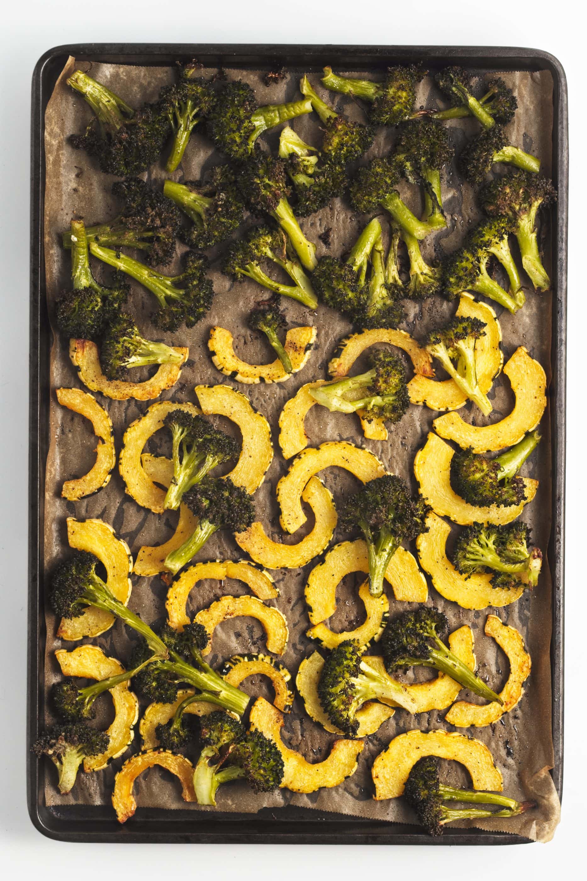 Roasted broccoli and delicata squash on a baking sheet.