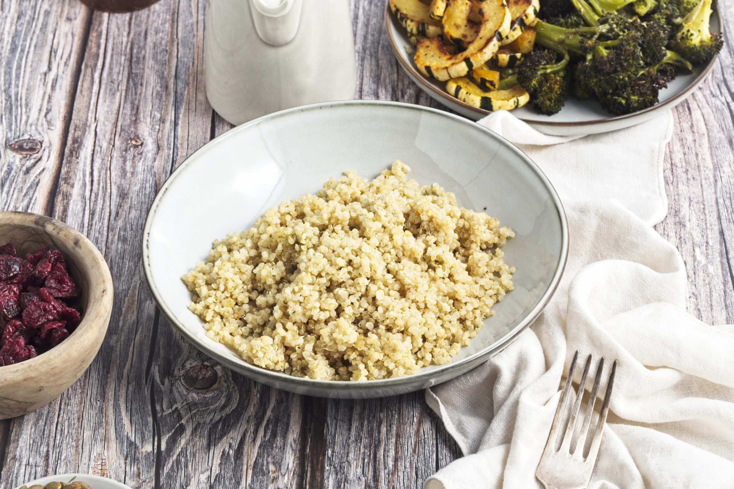 Cooked quinoa in a bowl with roasted broccoli and squash next to it on a plate.