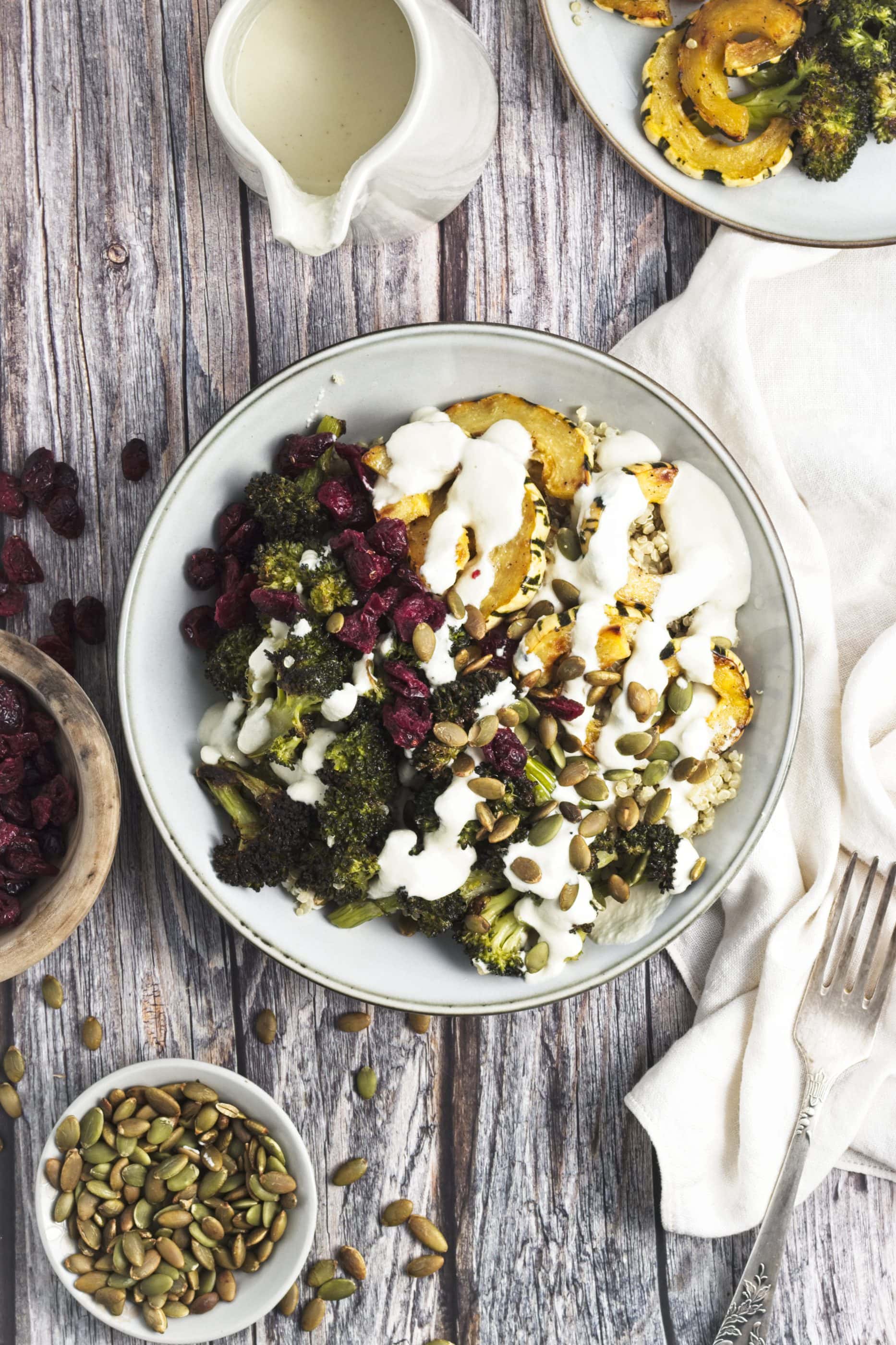 Quinoa with roasted broccoli and squash on top in a bowl with cashew dressing drizzled on top.