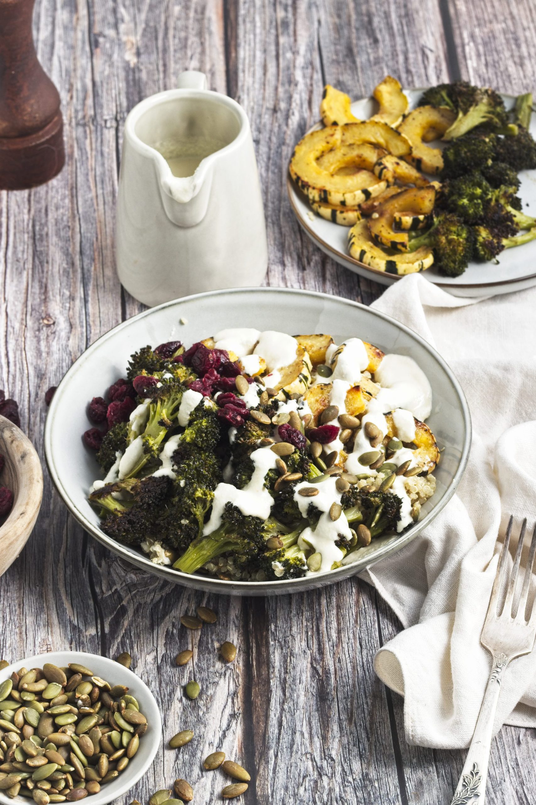 Quinoa with roasted broccoli and squash on top in a bowl with cashew dressing and pumpkin seeds drizzled on top.