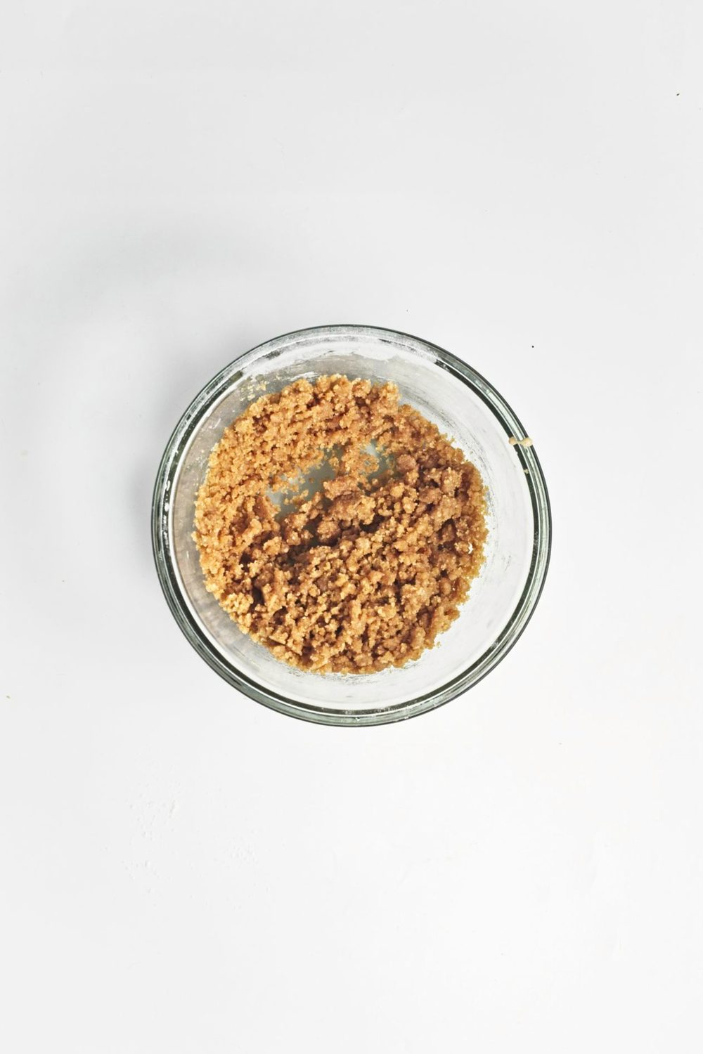 Ingredients mixed together creating a crumb topping for apple muffins in a glass bowl.