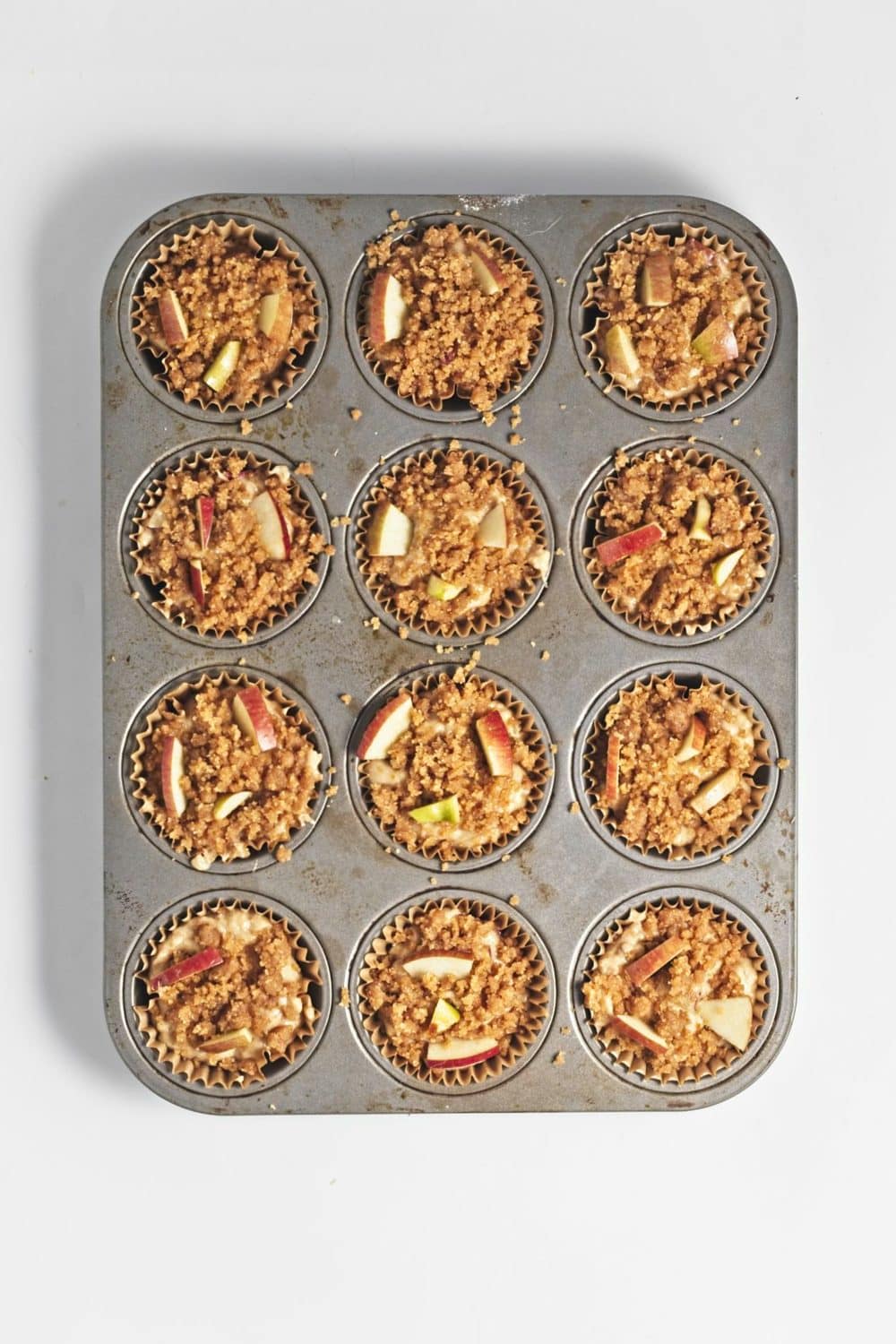 Apple crumb muffin batter with chopped apples and crumb topping in lined muffin tins.