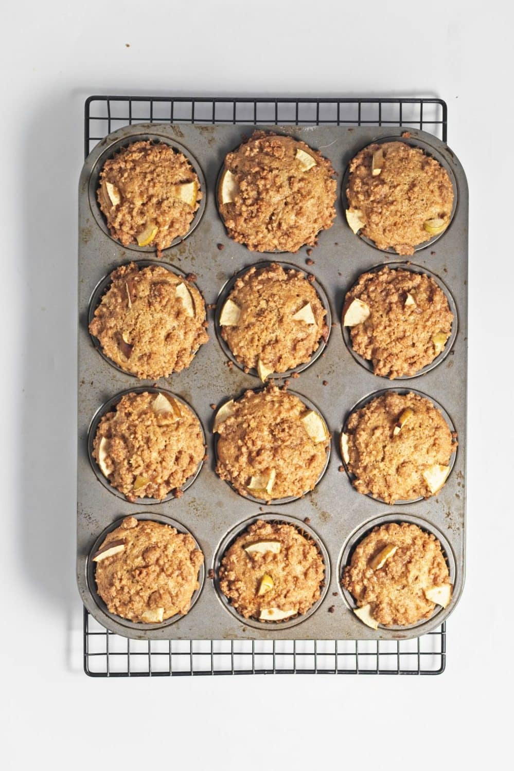 Cooked apple crumb muffins with chopped apples and crumb topping in lined muffin tins.