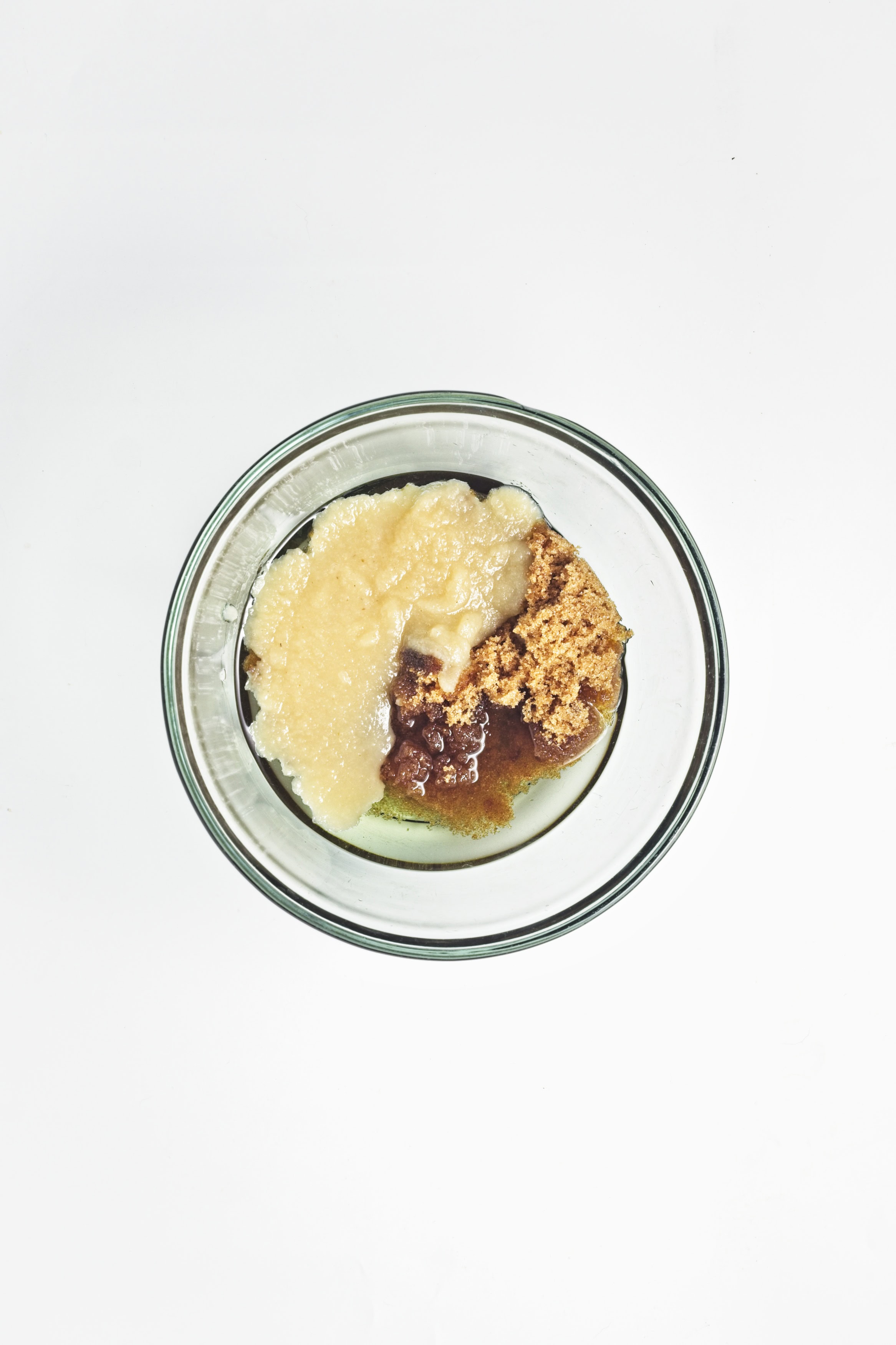 Wet ingredients for vegan apple crumb muffins, including applesauce, brown sugar, oil, and vanilla extract, measured in a clear glass bowl.