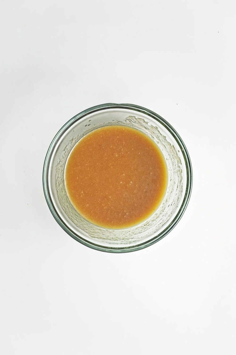 A glass mixing bowl filled with a smooth, golden brown wet mixture for homemade vegan apple crumb muffins, ready to combine with the dry ingredients.