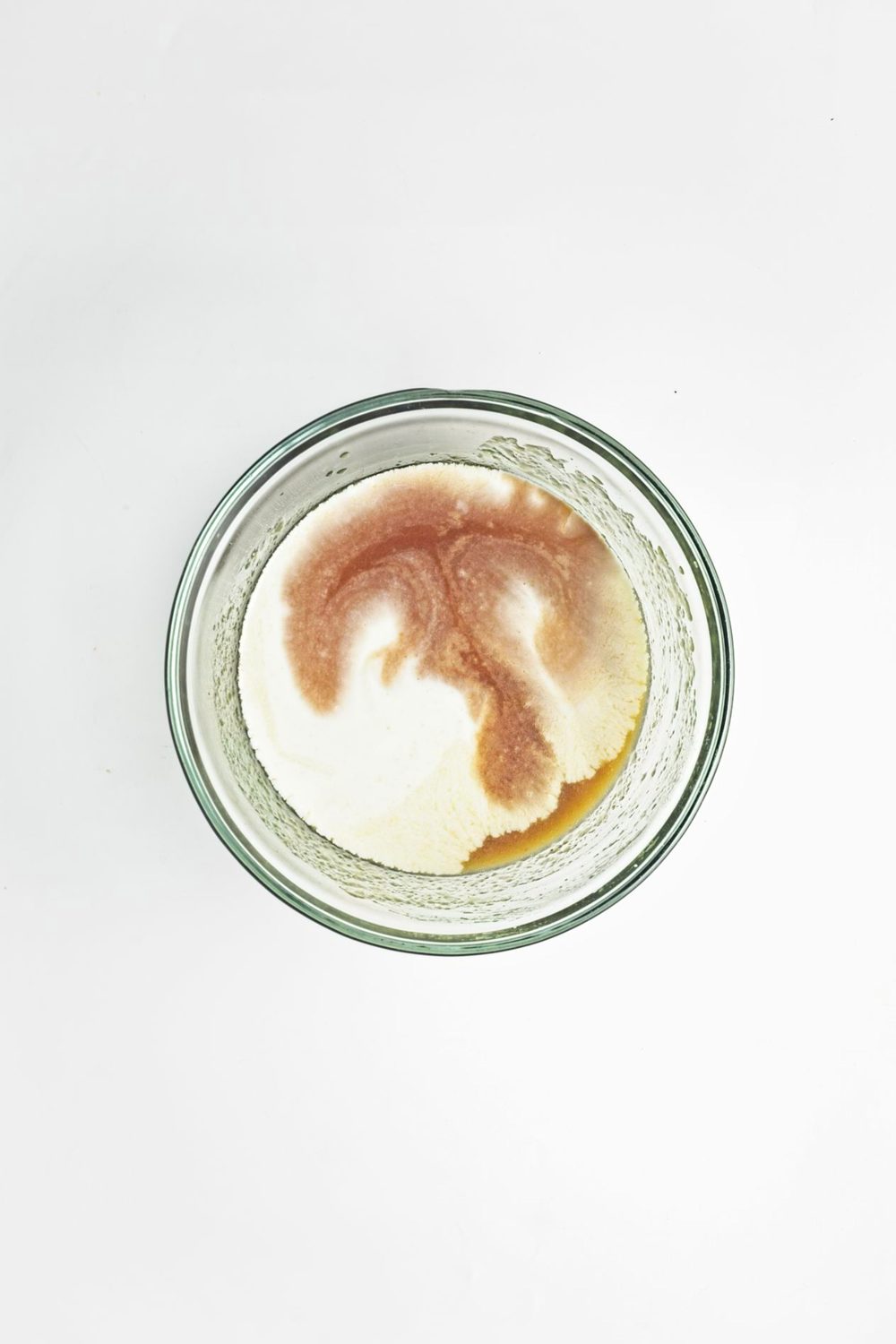 Adding almond milk and vanilla to the wet ingredients mixed together in a glass bowl.