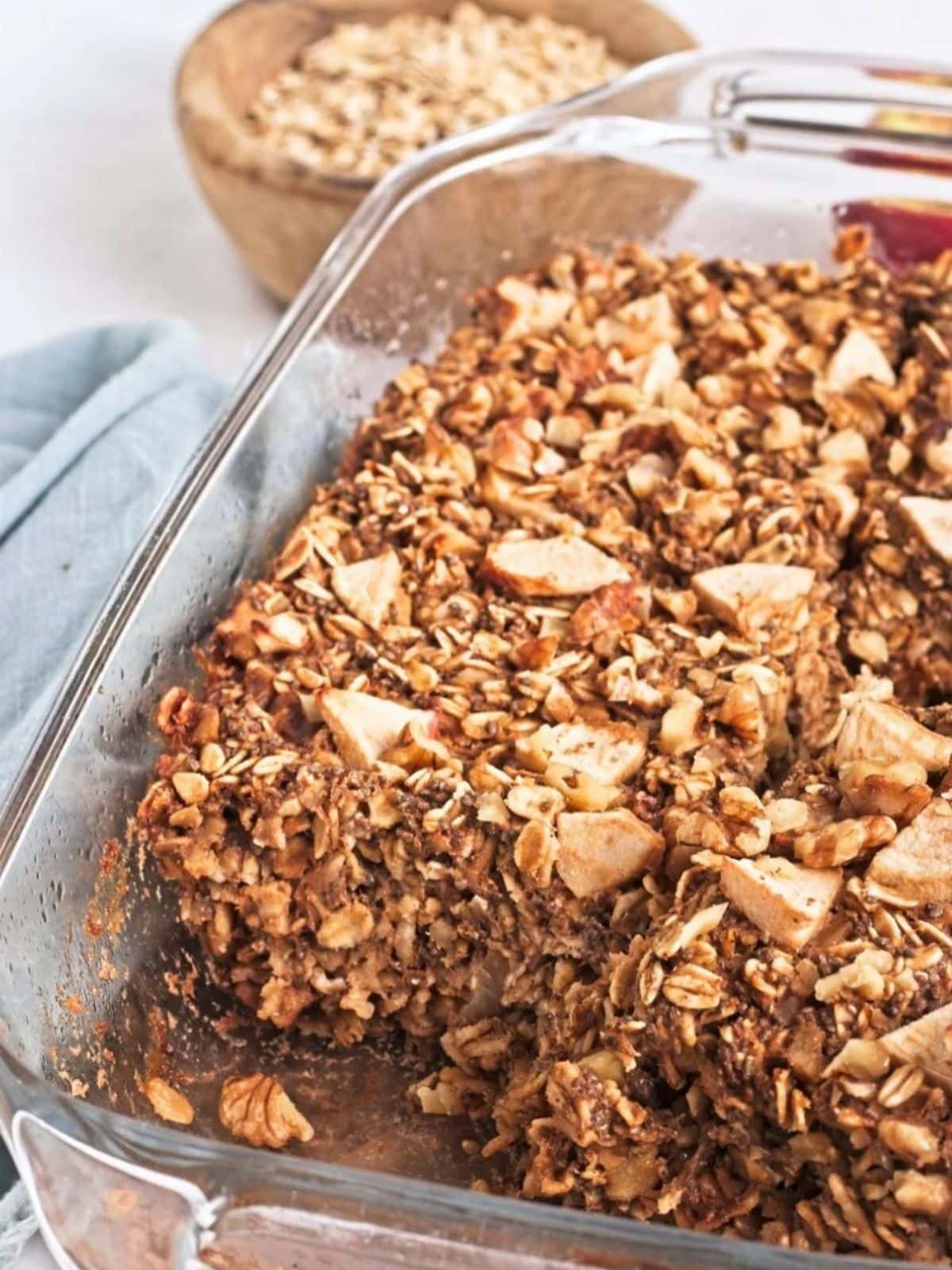 Vegan baked apple protein oatmeal in a glass baking dish, filled with rolled oats, chopped apples, walnuts, and warm cinnamon. This gluten-free baked oatmeal makes a hearty breakfast with protein and fiber.