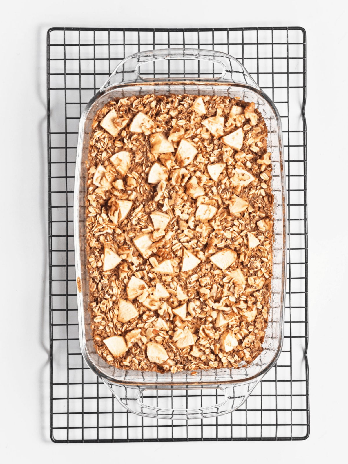 Overhead image of cooked vegan apple protein oatmeal with sliced apples on top in a baking dish on a wire rack.