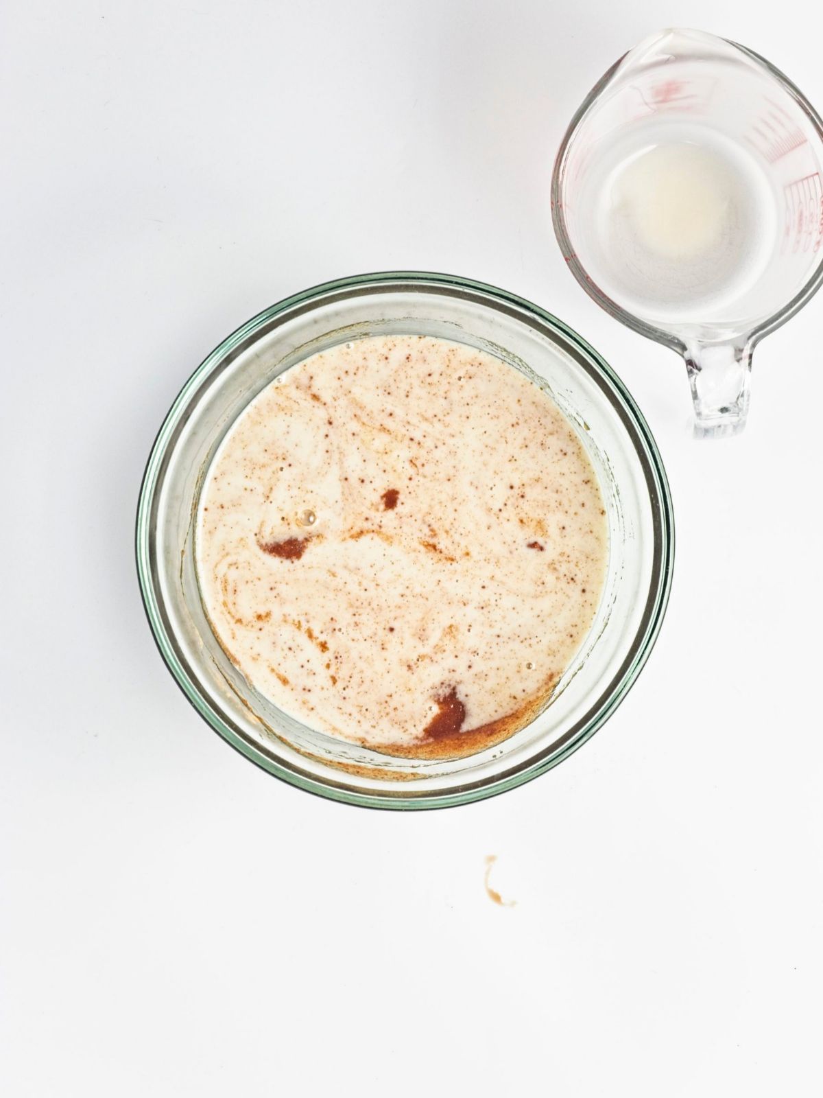 Plant-based milk poured into a glass bowl with cinnamon-spiced ingredients for vegan baked apple protein oatmeal, helping create a moist baked oatmeal texture.