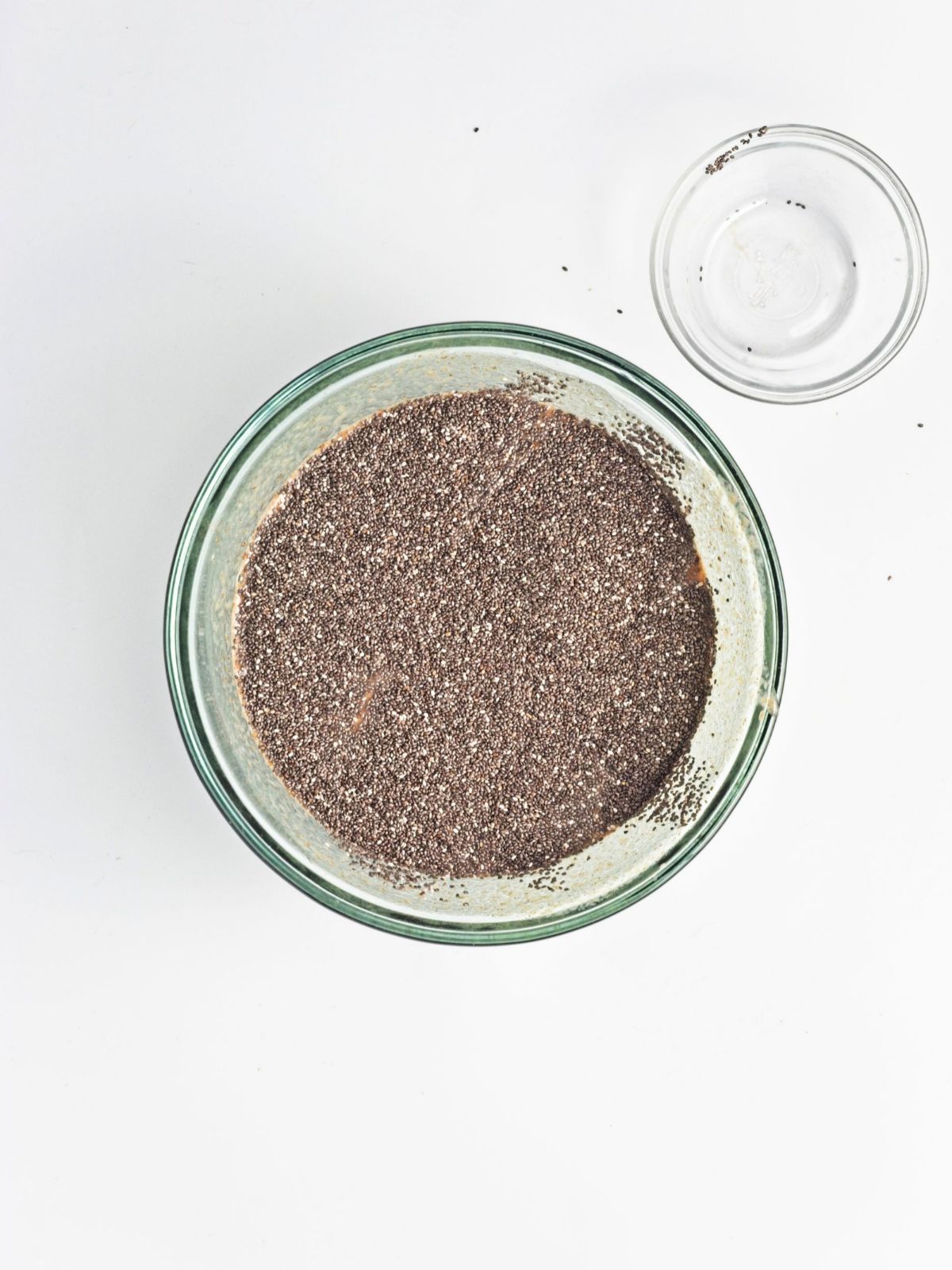 Chia seeds added to the wet mixture in a glass bowl for baked apple protein oatmeal, a vegan and gluten-free breakfast recipe with fiber and plant-based ingredients.